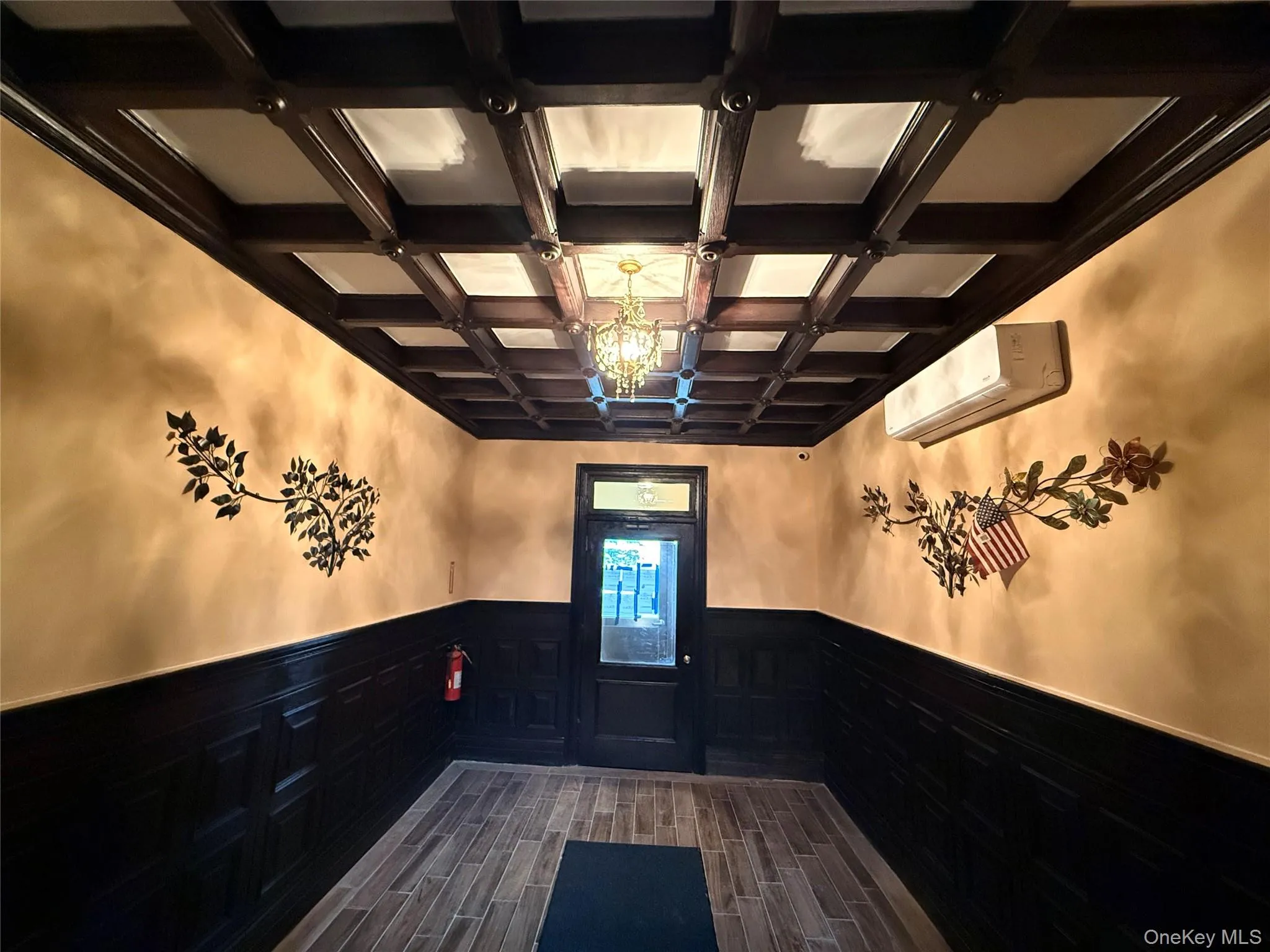 Doorway with coffered ceiling, wood finish floors, a wainscoted wall, and hanging lights Doorway with coffered ceiling, wood finish floors, a wainscoted wall, and hanging lights