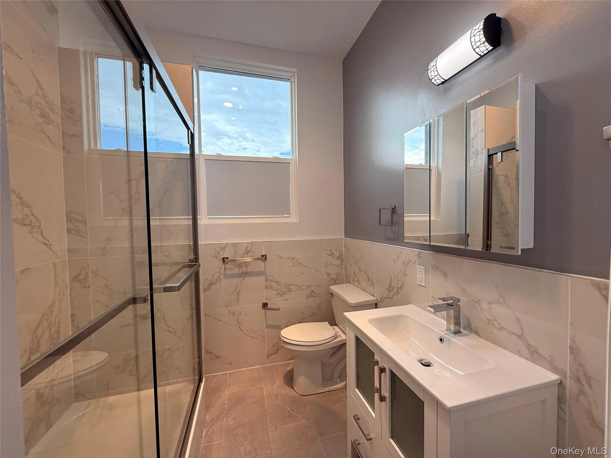 Full bathroom with tile walls, wainscoting, vanity, and a marble finish shower Full bathroom with tile walls, wainscoting, vanity, and a marble finish shower