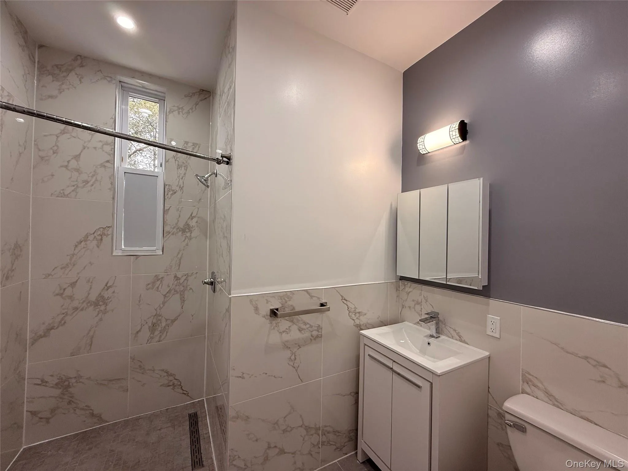Full bathroom featuring vanity, a marble finish shower, tile walls, and a wainscoted wall Full bathroom featuring vanity, a marble finish shower, tile walls, and a wainscoted wall