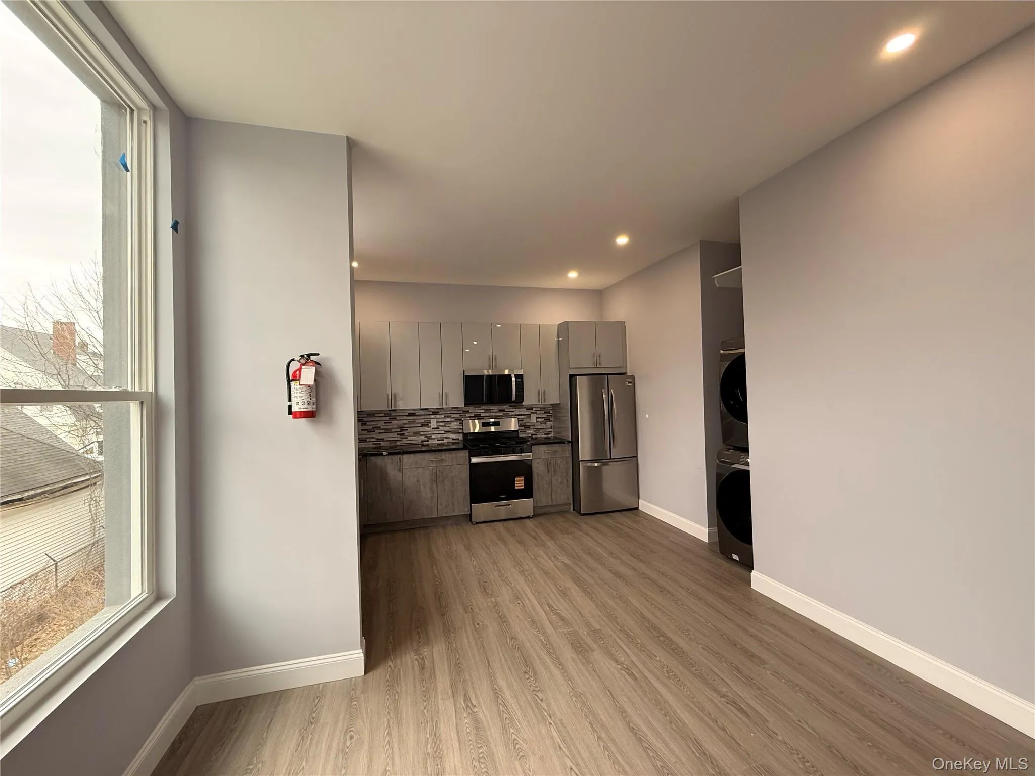 Kitchen featuring stainless steel appliances, gray cabinets, light wood finished floors, dark countertops, and stacked washer / drying machine Kitchen featuring stainless steel appliances, gray cabinets, light wood finished floors, dark countertops, and stacked washer / drying machine