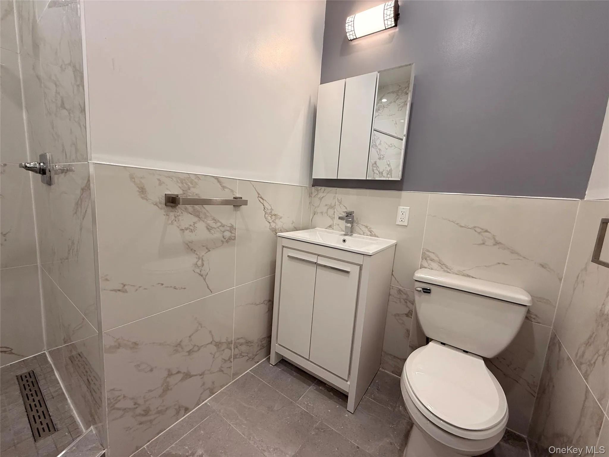 Full bathroom with vanity, a marble finish shower, tile walls, and a wainscoted wall Full bathroom with vanity, a marble finish shower, tile walls, and a wainscoted wall