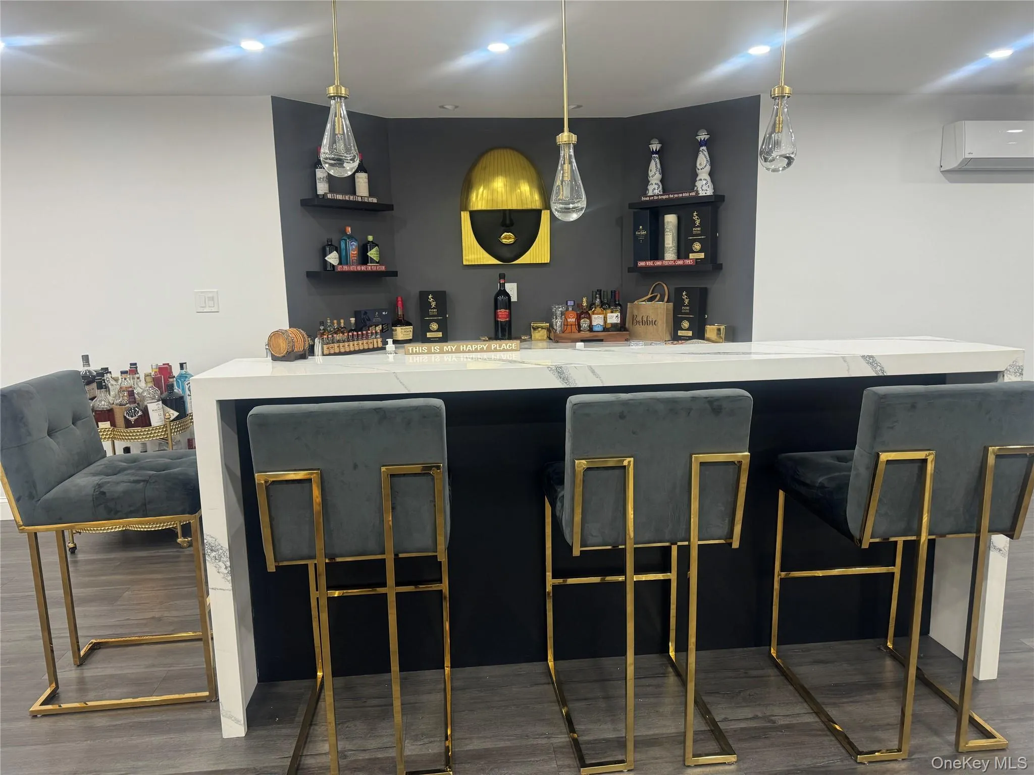 Indoor bar featuring dark wood-style floors, open shelves, light stone countertops, and decorative light fixtures Indoor bar featuring dark wood-style floors, open shelves, light stone countertops, and decorative light fixtures