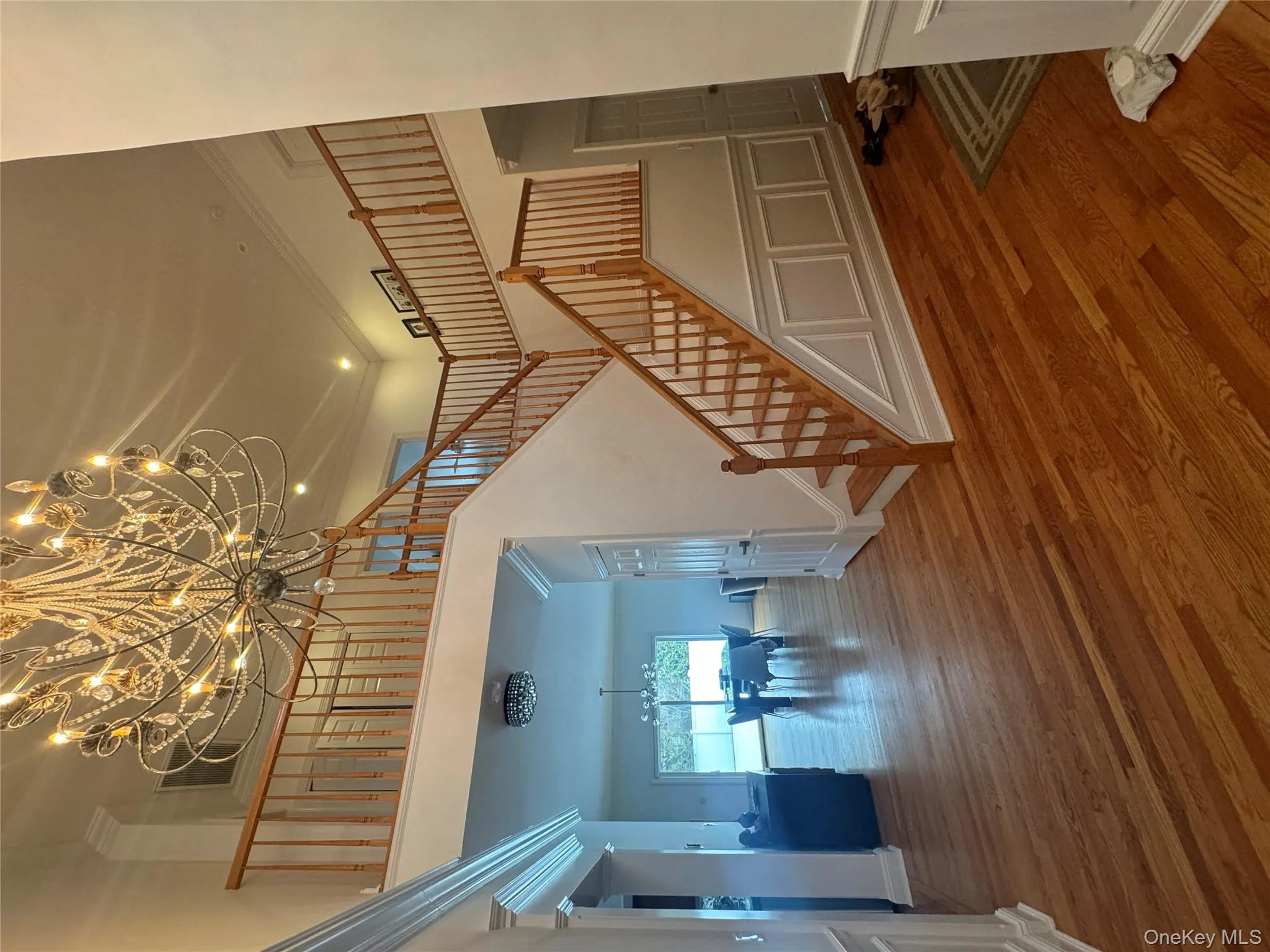 Stairway with a chandelier, crown molding, a decorative wall, wood finished floors, and a high ceiling Stairway with a chandelier, crown molding, a decorative wall, wood finished floors, and a high ceiling