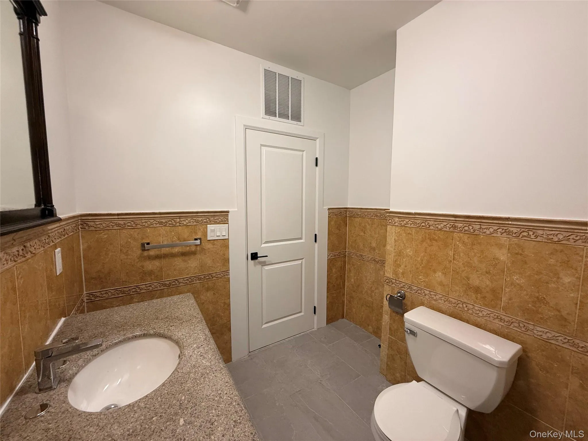 Bathroom with vanity, a wainscoted wall, tile walls, and dark tile patterned floors Bathroom with vanity, a wainscoted wall, tile walls, and dark tile patterned floors