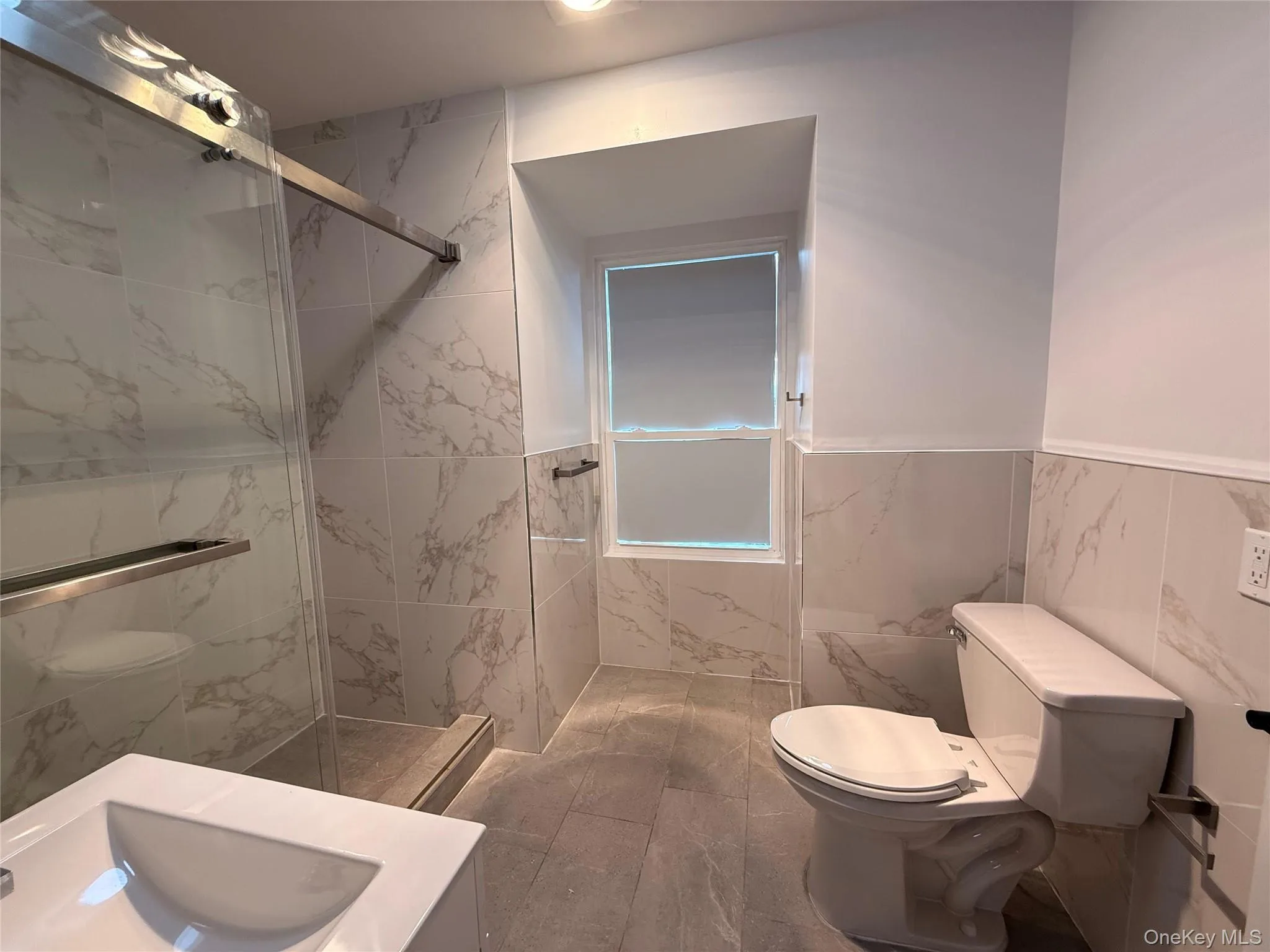 Bathroom featuring a marble finish shower, tile walls, vanity, and a wainscoted wall Bathroom featuring a marble finish shower, tile walls, vanity, and a wainscoted wall