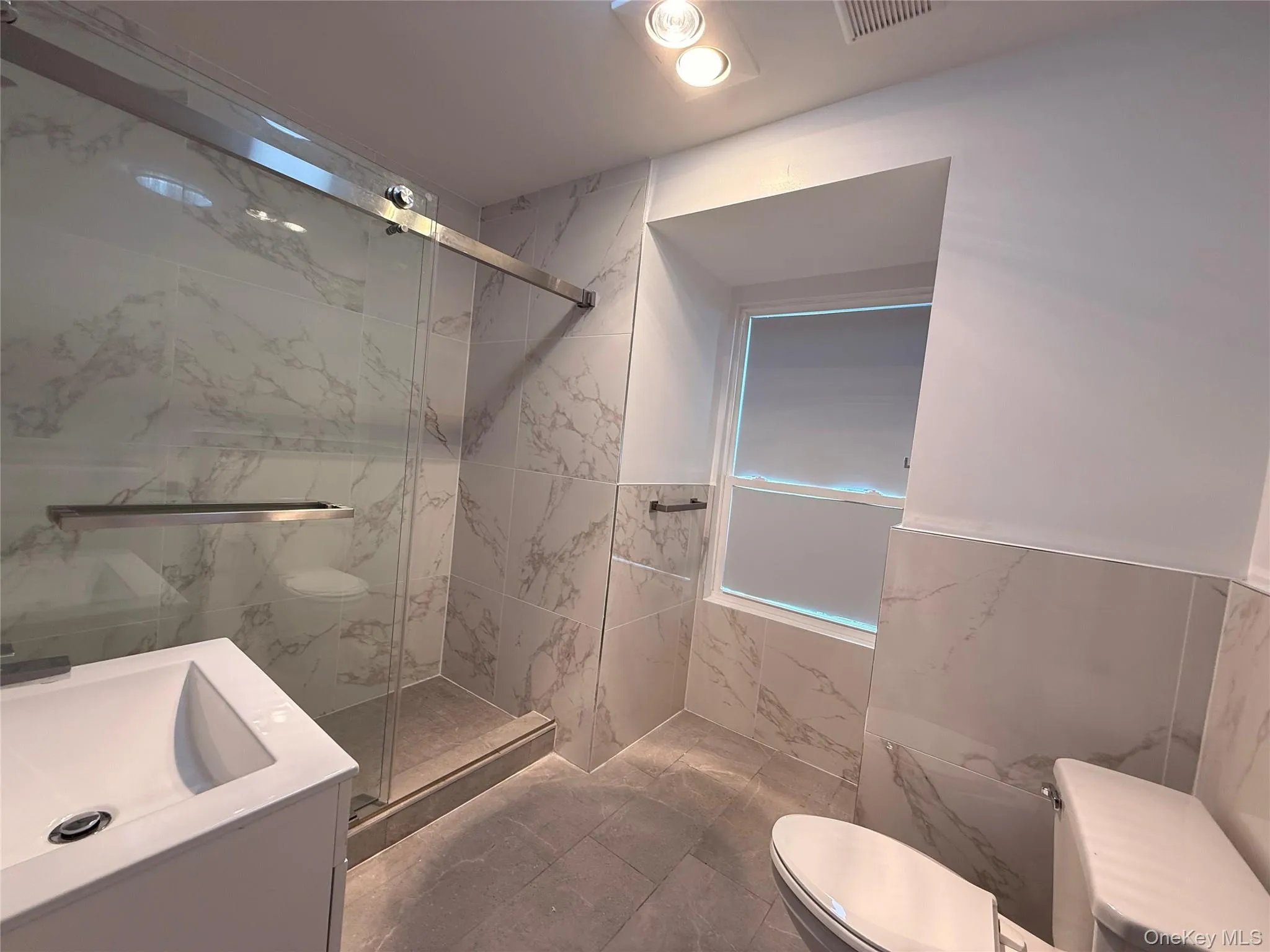 Bathroom featuring vanity, a marble finish shower, tile walls, and wainscoting Bathroom featuring vanity, a marble finish shower, tile walls, and wainscoting
