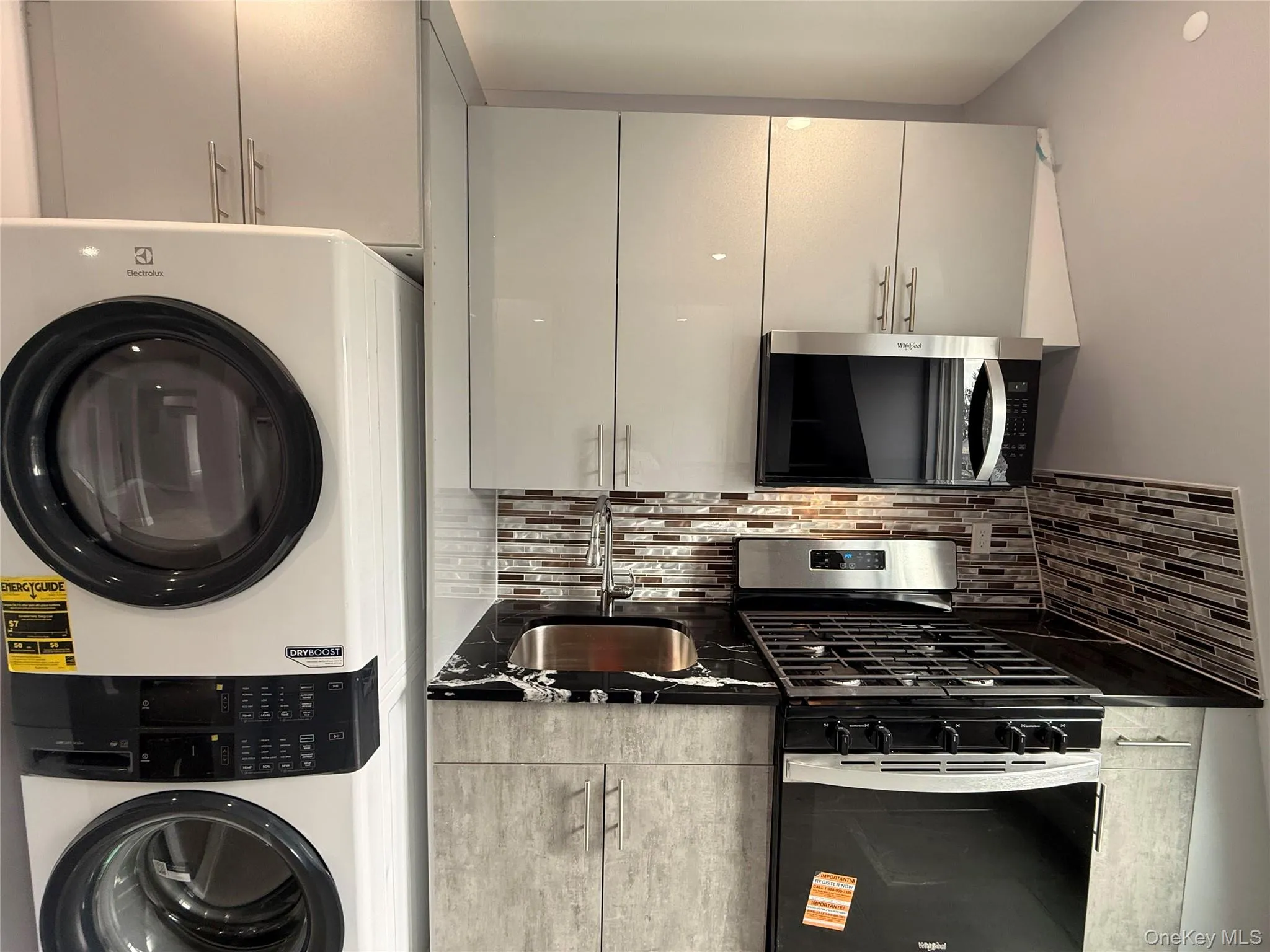 Kitchen with stainless steel appliances, stacked washing machine and dryer, tasteful backsplash, and dark stone counters Kitchen with stainless steel appliances, stacked washing machine and dryer, tasteful backsplash, and dark stone counters