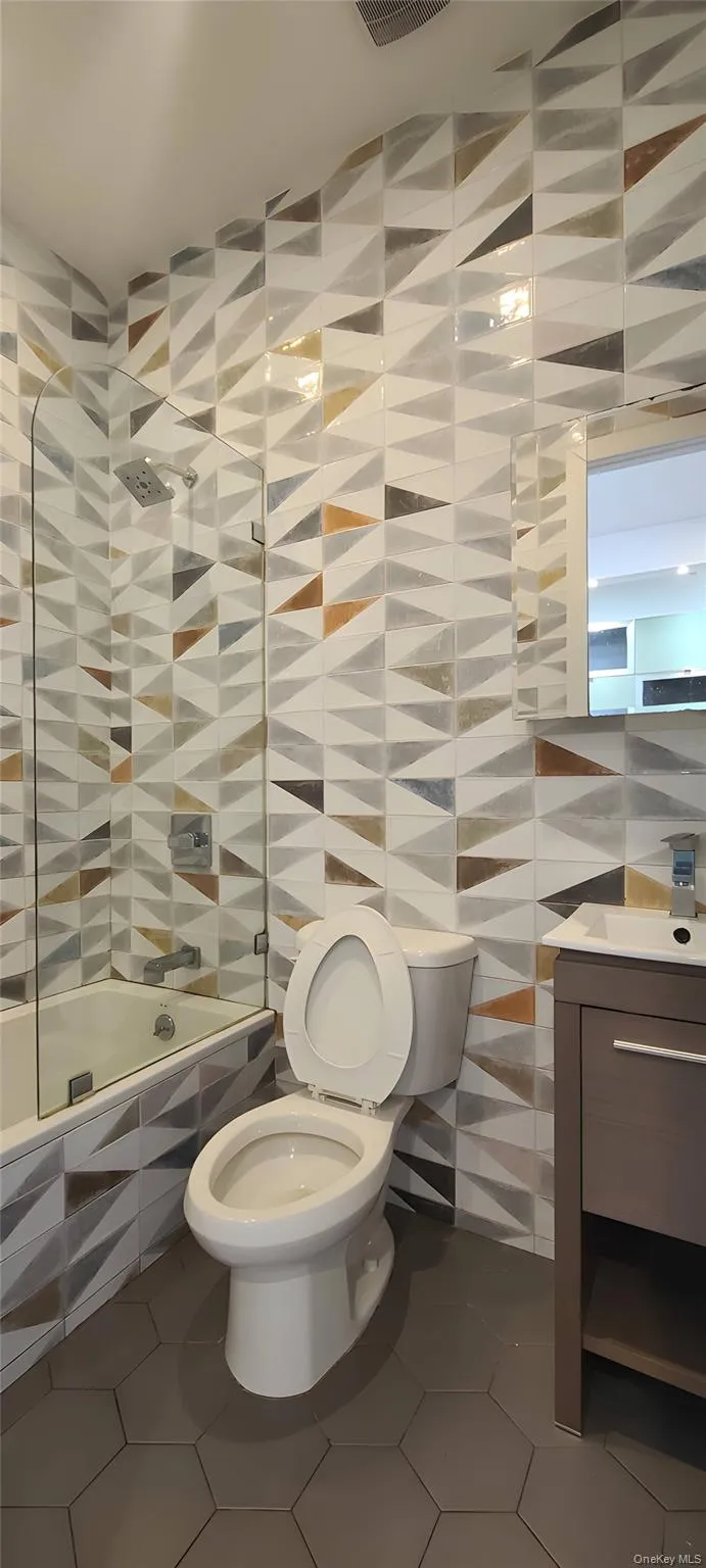 Full bath with vanity, tile walls, tiled shower / bath combo, and dark tile patterned flooring Full bath with vanity, tile walls, tiled shower / bath combo, and dark tile patterned flooring