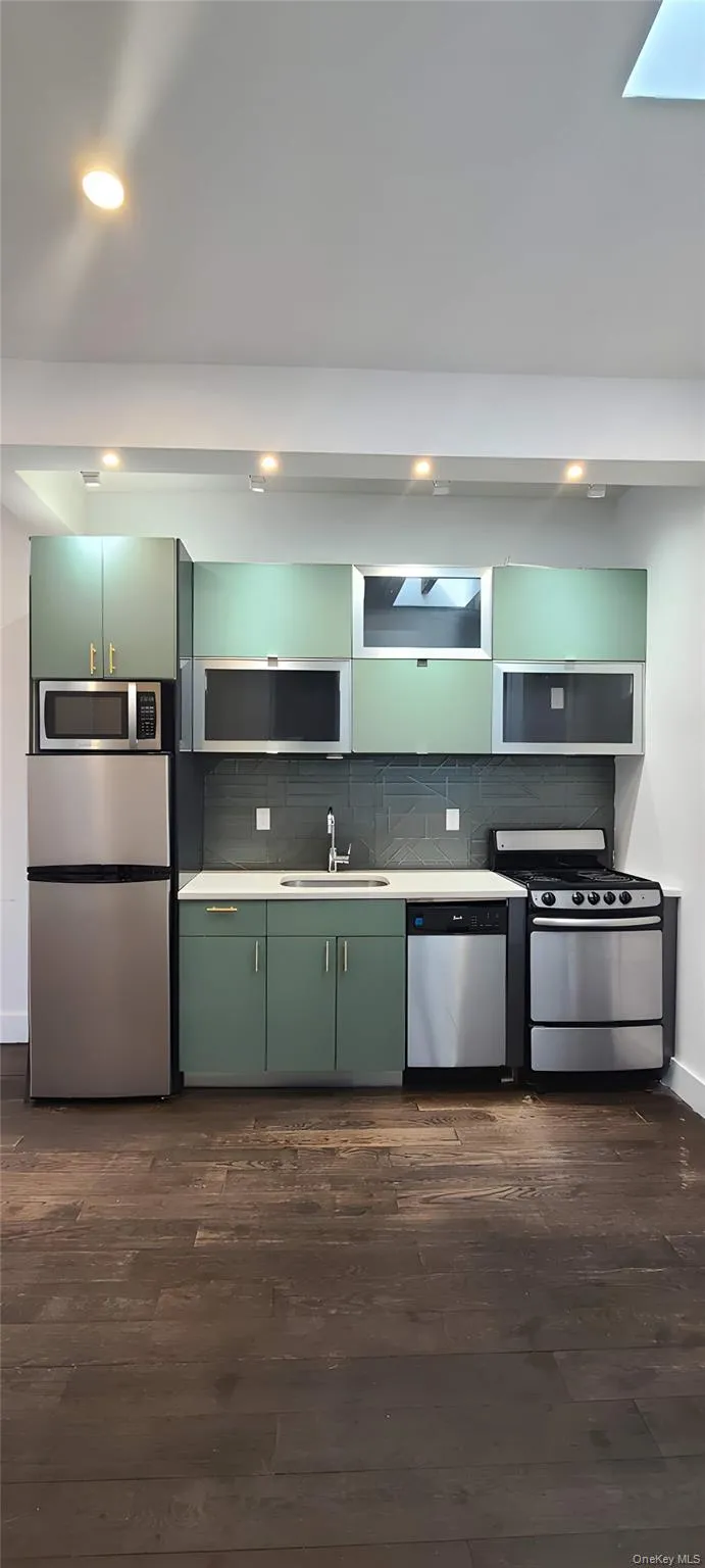 Kitchen with green cabinets, dark wood-style floors, stainless steel appliances, light countertops, and recessed lighting Kitchen with green cabinets, dark wood-style floors, stainless steel appliances, light countertops, and recessed lighting