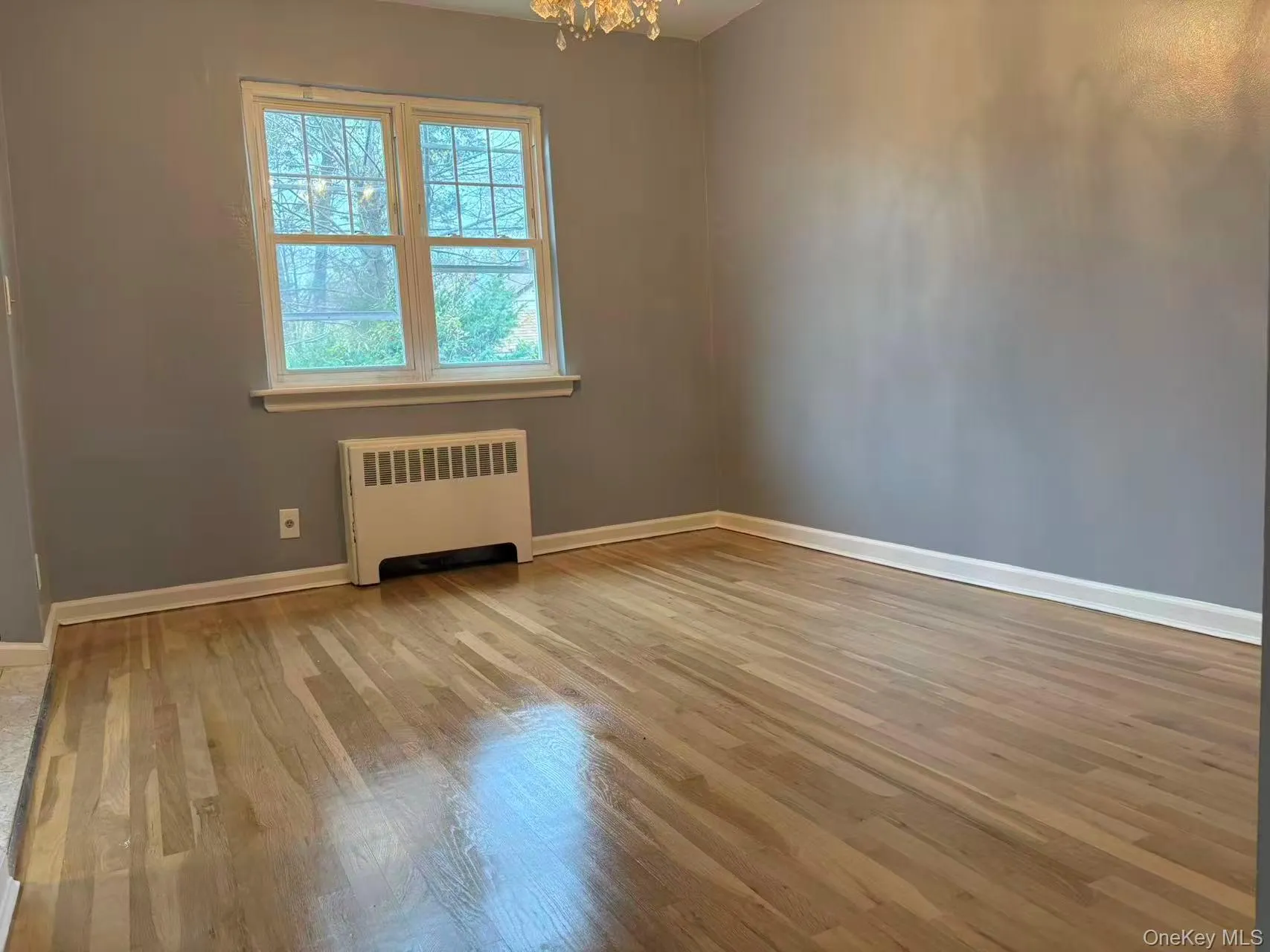 Empty room featuring radiator heating unit, light wood-style flooring, and a chandelier Empty room featuring radiator heating unit, light wood-style flooring, and a chandelier