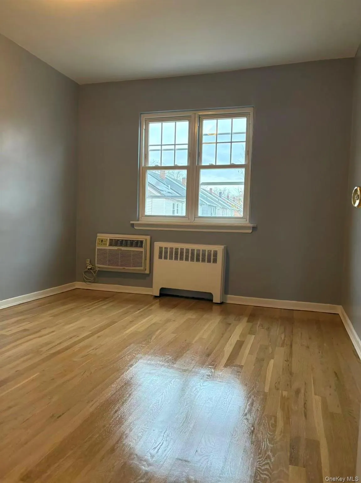 Unfurnished room featuring radiator heating unit, light wood-style flooring, and a wall mounted air conditioner Unfurnished room featuring radiator heating unit, light wood-style flooring, and a wall mounted air conditioner