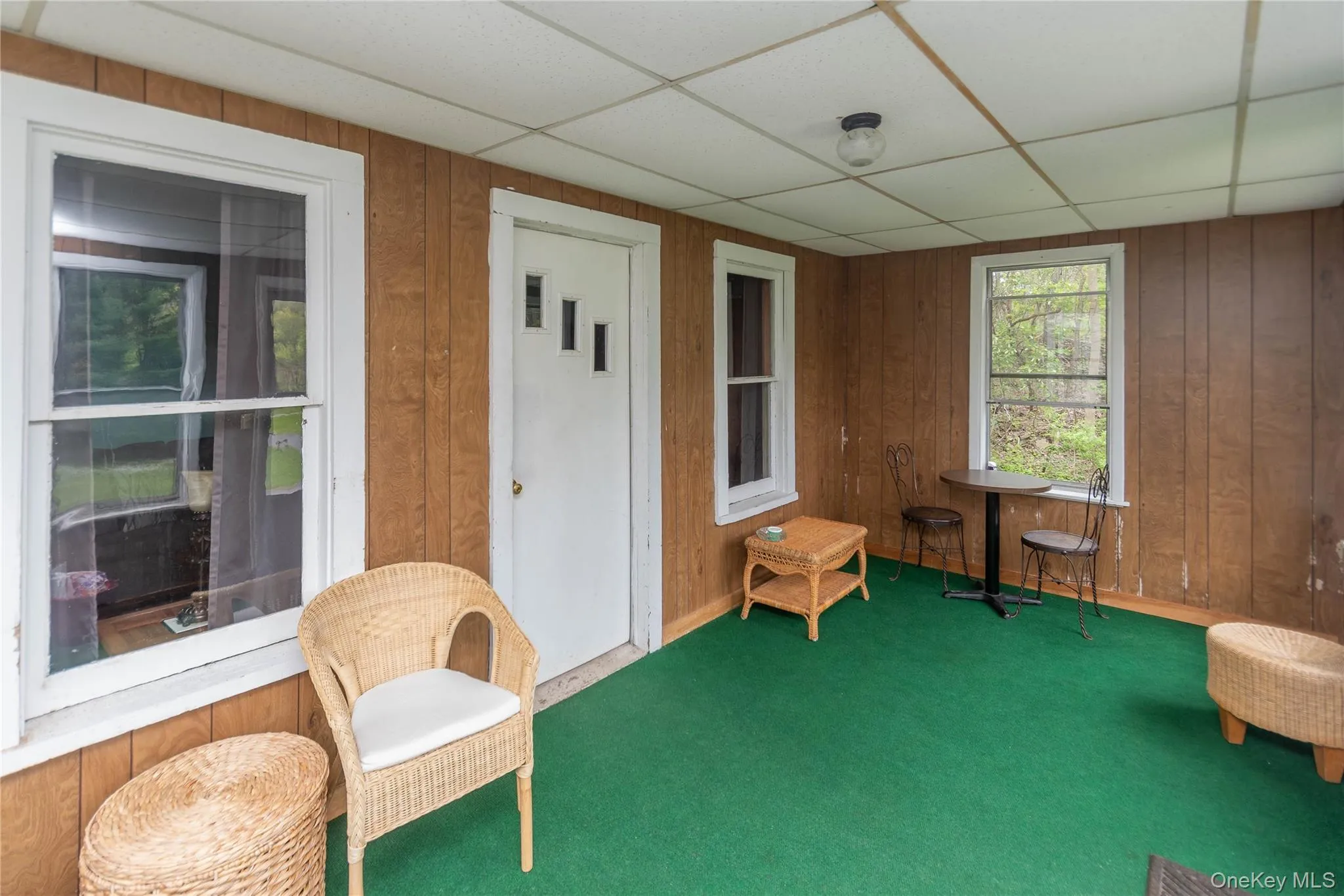 Enclosed porch featuring wood-panel walls, multiple windows, and a grid-patterned ceiling Enclosed porch featuring wood-panel walls, multiple windows, and a grid-patterned ceiling