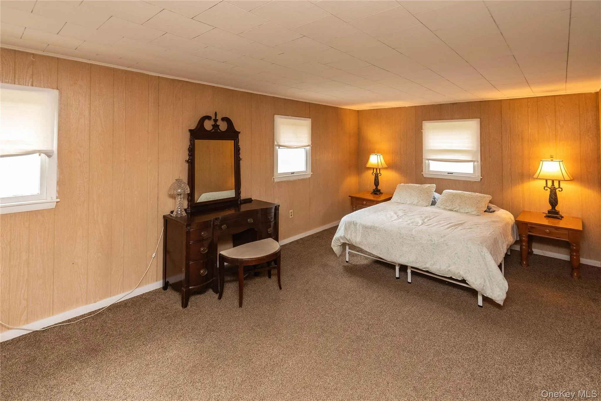 Room featuring wood-paneled walls, multiple windows with white blinds, and a neutral-toned carpet Room featuring wood-paneled walls, multiple windows with white blinds, and a neutral-toned carpet