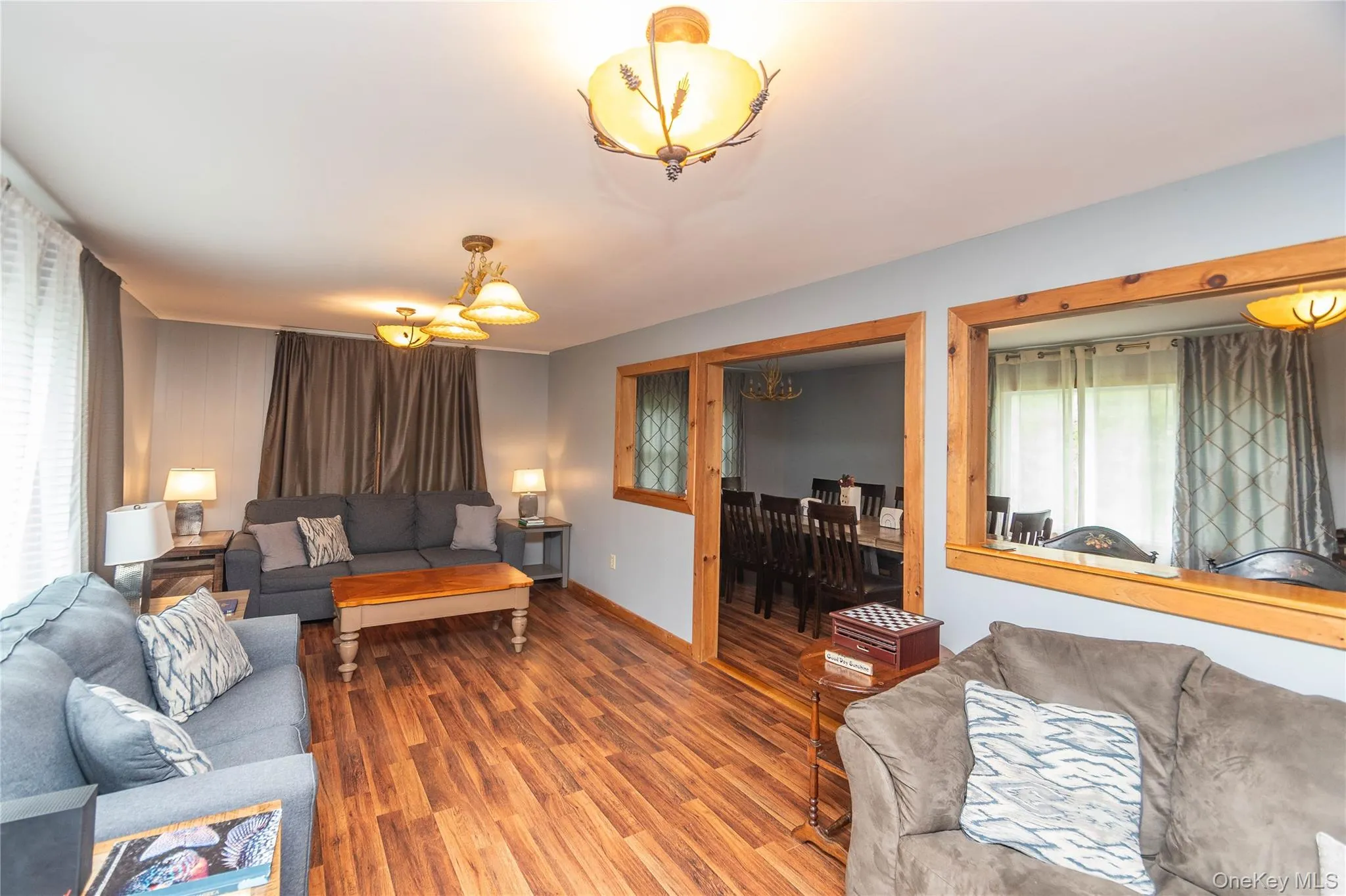 Spacious living area featuring wood-finish flooring, light blue wall paint, and multiple ceiling light fixtures Spacious living area featuring wood-finish flooring, light blue wall paint, and multiple ceiling light fixtures