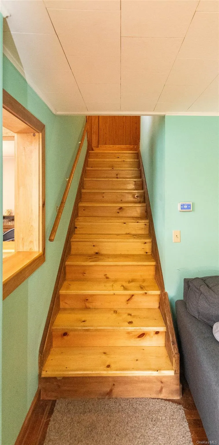 Natural wood staircase with matching railing, wood-trim window opening, and light green wall paint Natural wood staircase with matching railing, wood-trim window opening, and light green wall paint