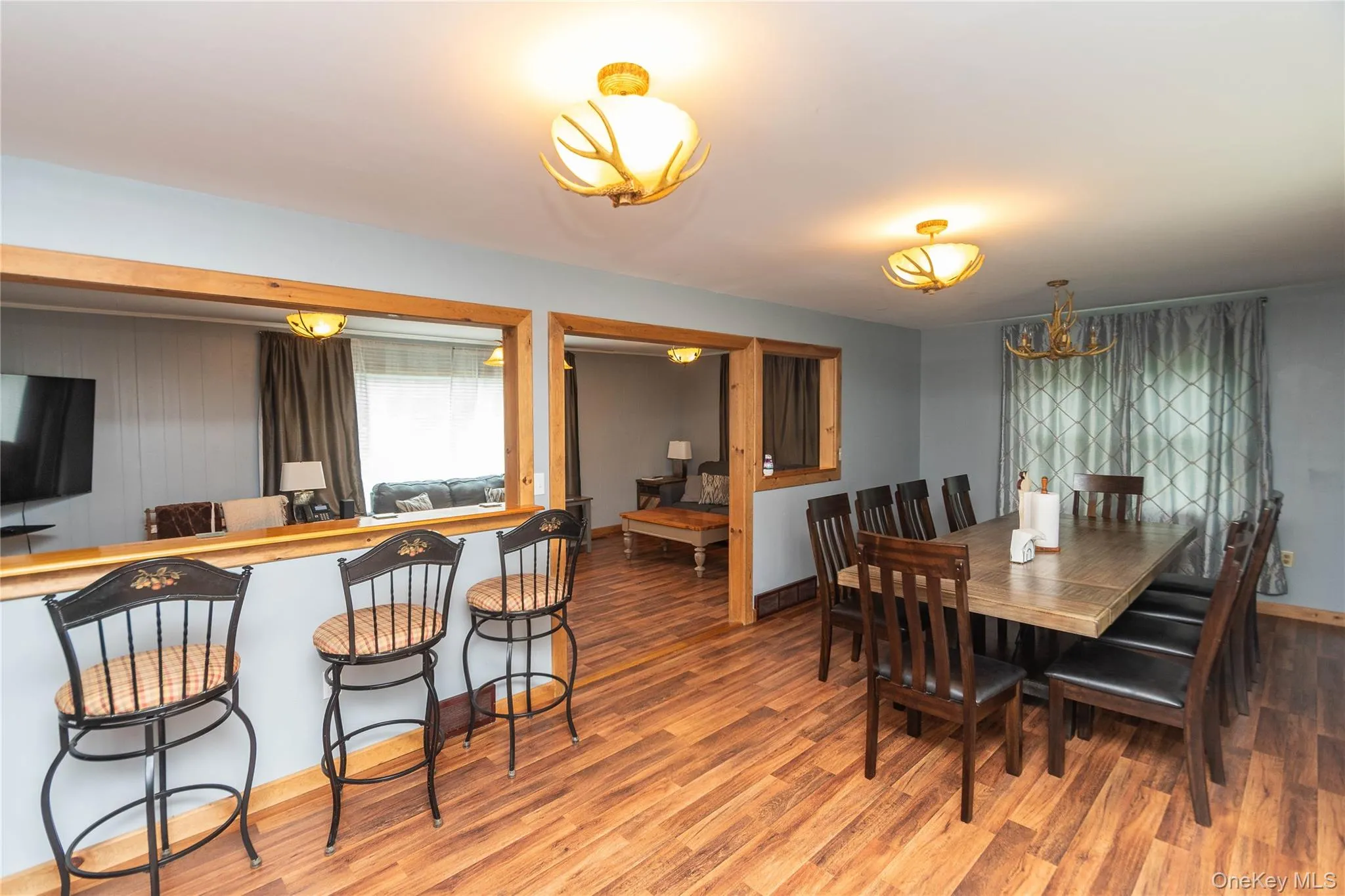 Open-concept living area featuring wood-finish flooring, a dining space with a chandelier, and a breakfast bar with decorative lighting Open-concept living area featuring wood-finish flooring, a dining space with a chandelier, and a breakfast bar with decorative lighting