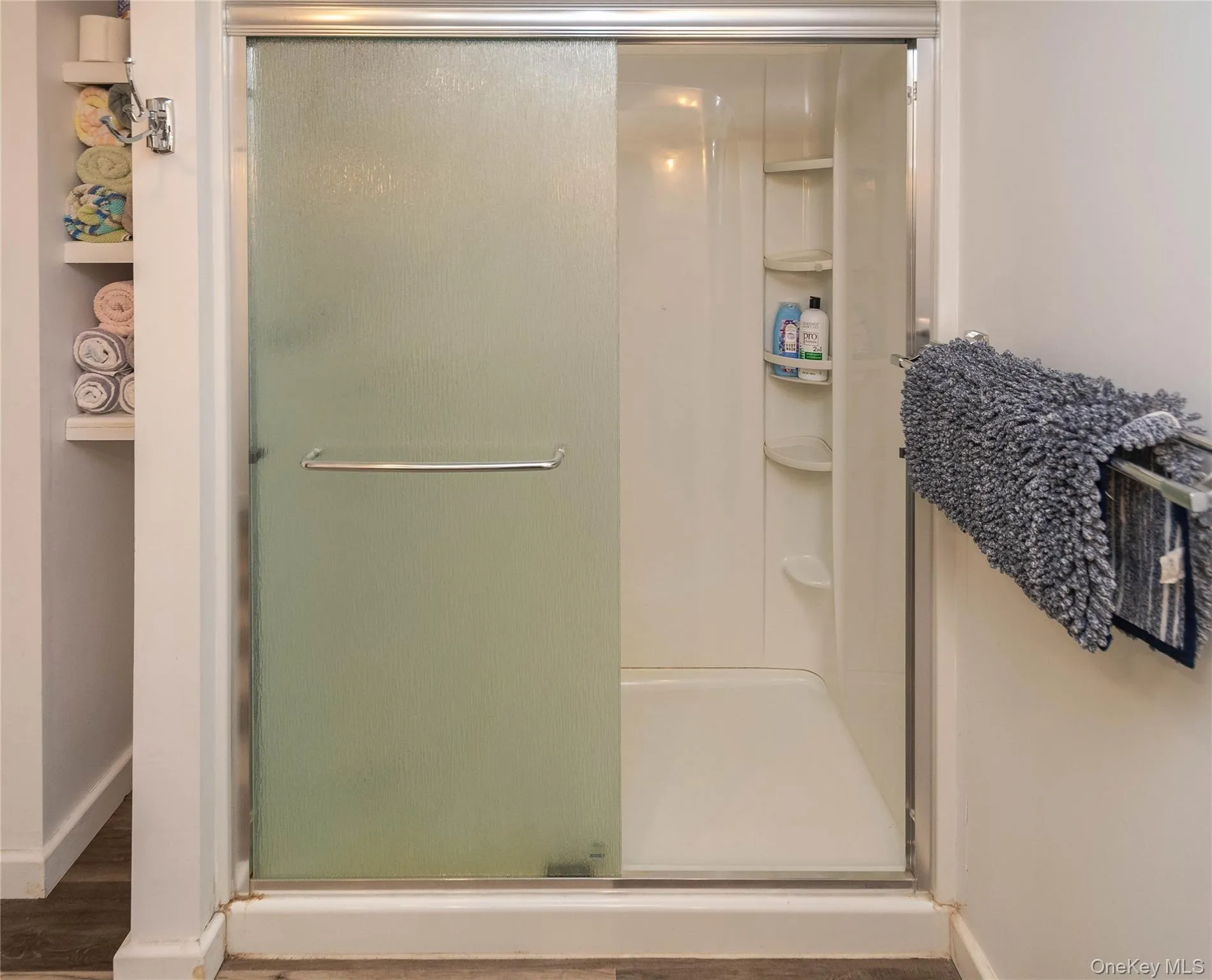 Shower enclosure with frosted glass sliding door, integrated shelving, and white base Shower enclosure with frosted glass sliding door, integrated shelving, and white base