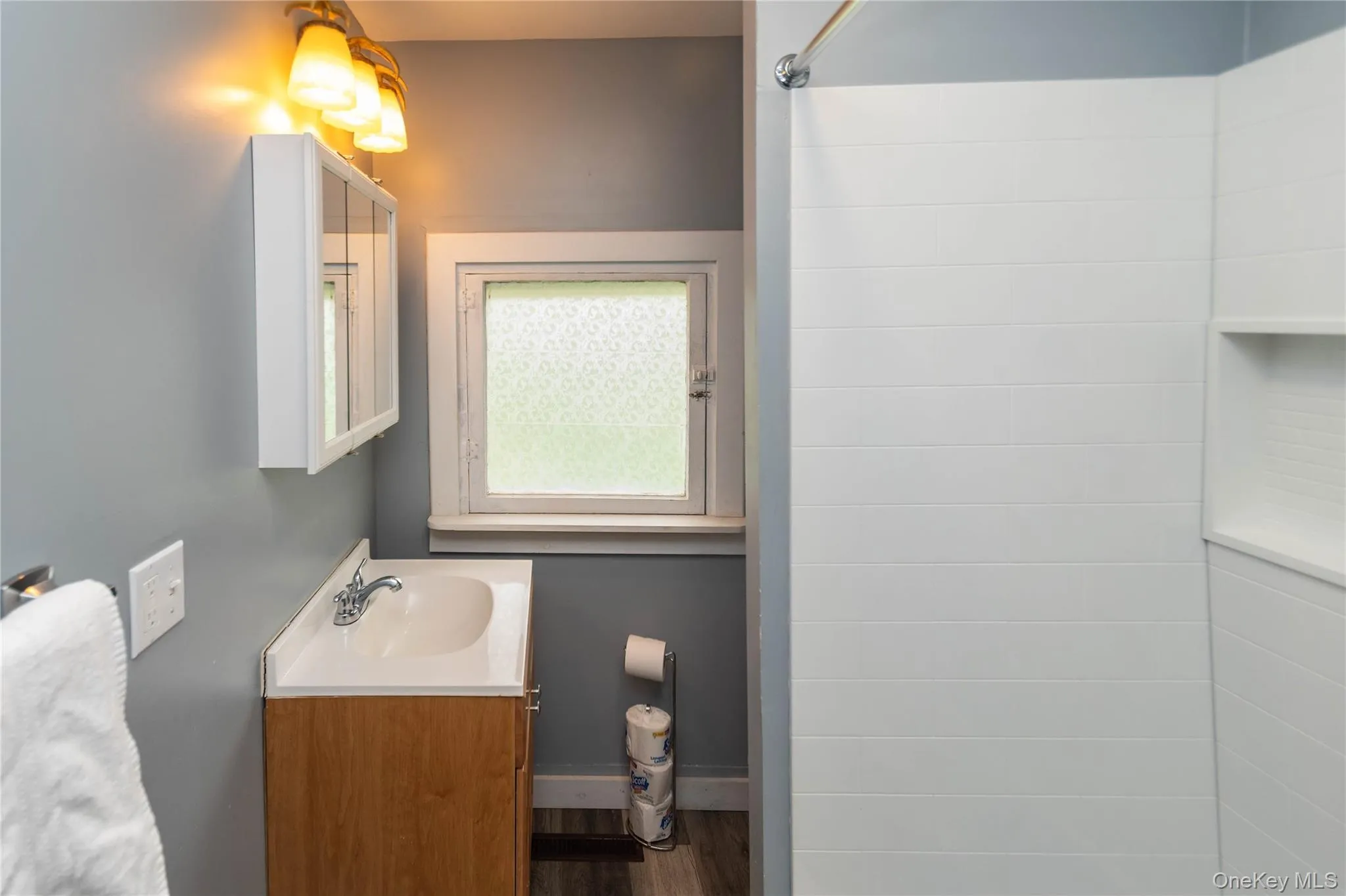 Compact bathroom featuring a wood-finish vanity with an integrated sink, a medicine cabinet, and a tiled shower with a built-in niche Compact bathroom featuring a wood-finish vanity with an integrated sink, a medicine cabinet, and a tiled shower with a built-in niche