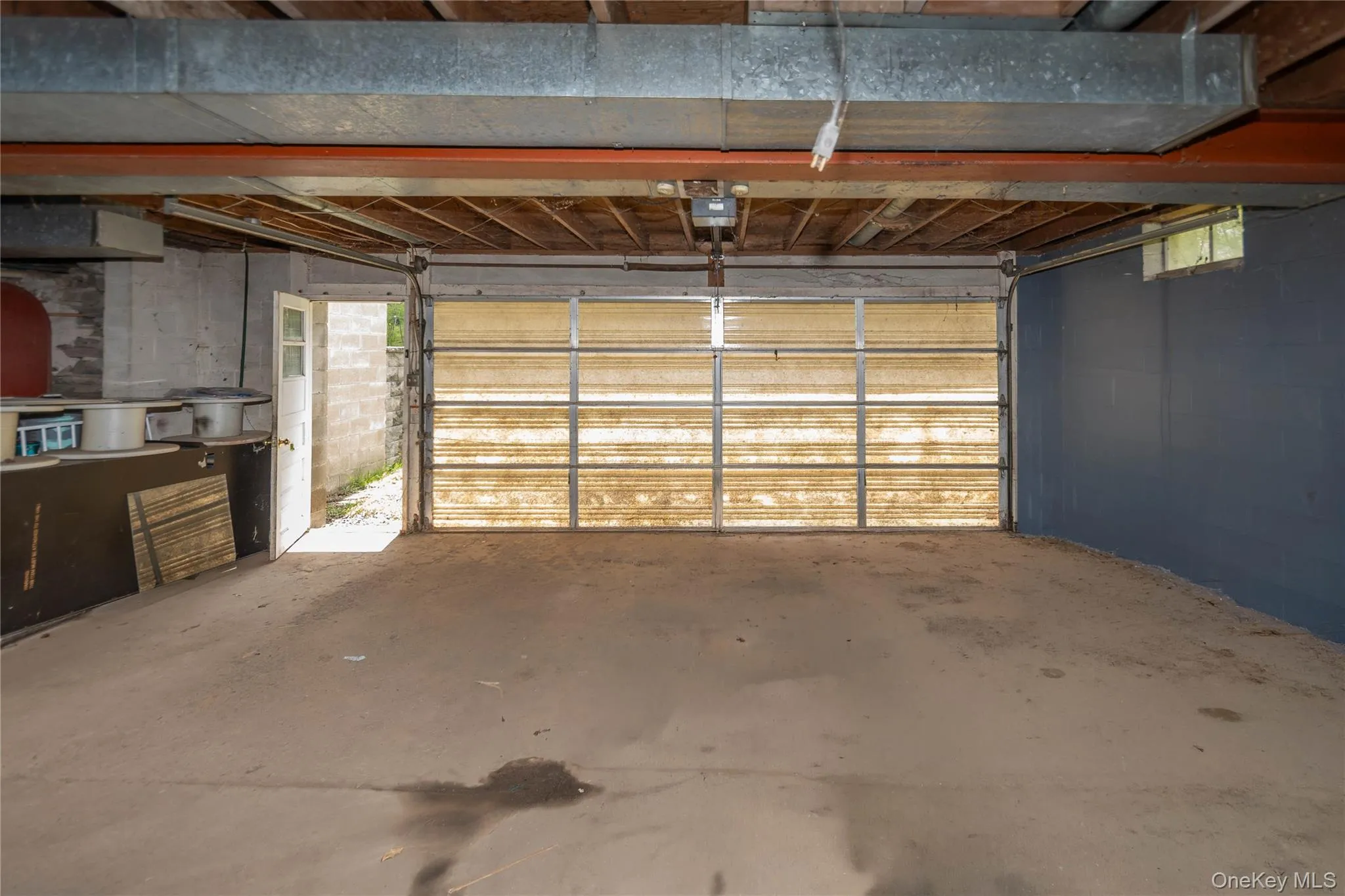 Garage space featuring a translucent overhead door, concrete flooring, exposed ceiling joists, and a painted cinder block wall Garage space featuring a translucent overhead door, concrete flooring, exposed ceiling joists, and a painted cinder block wall