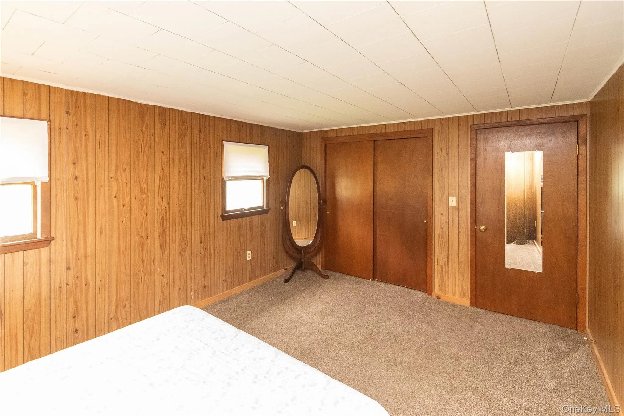 Room featuring wood-paneled walls, two windows with blinds, and light-colored ceiling panels Room featuring wood-paneled walls, two windows with blinds, and light-colored ceiling panels
