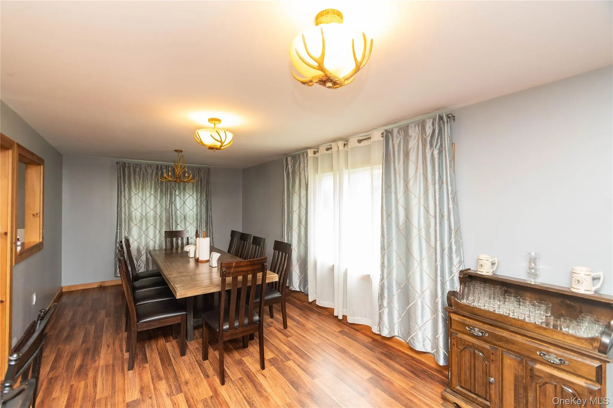 Spacious room featuring wood-finish flooring, light grey walls, and two windows with drapes Spacious room featuring wood-finish flooring, light grey walls, and two windows with drapes