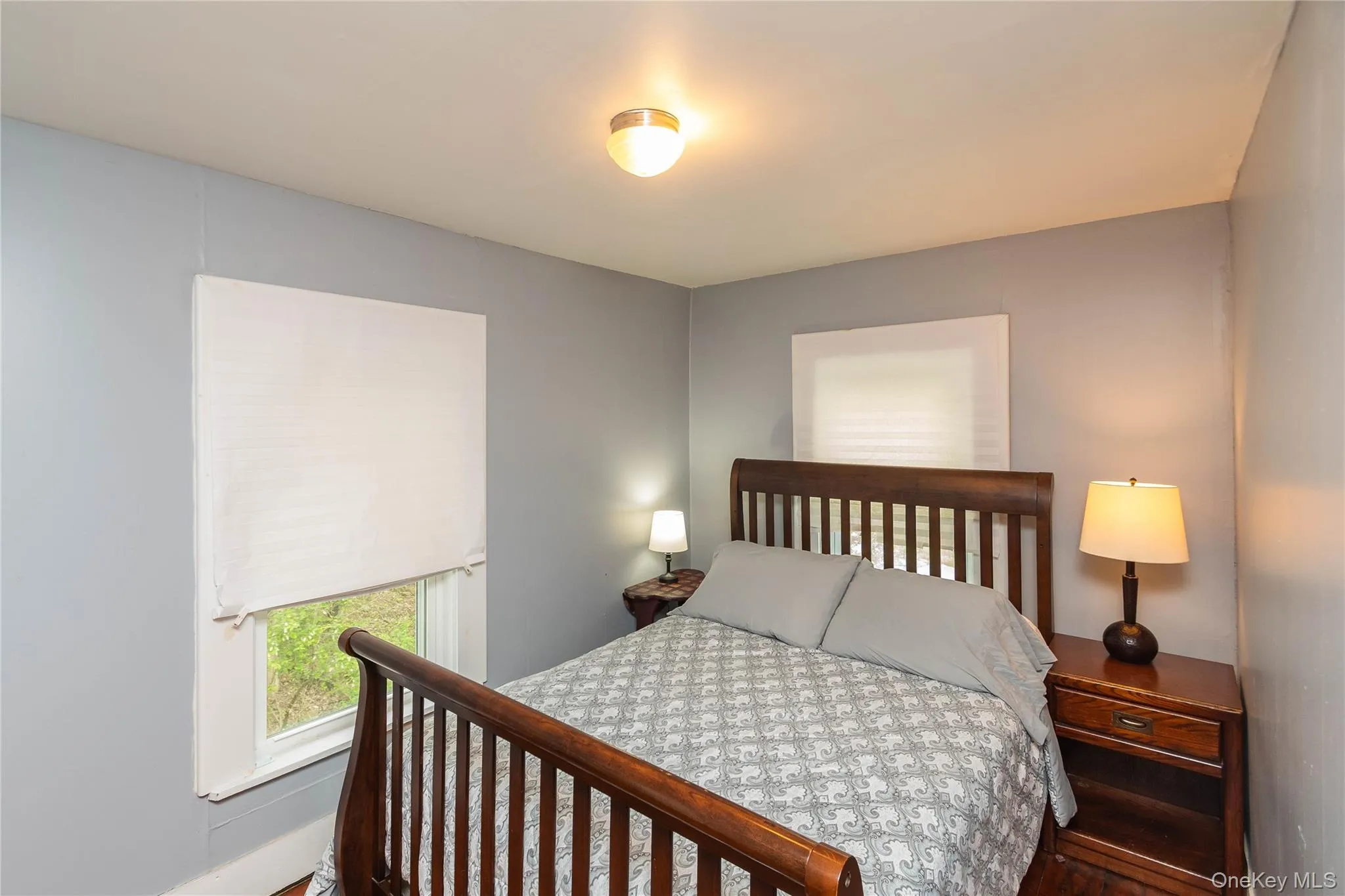 Bedroom featuring light gray walls, white trim, and two windows with white shades Bedroom featuring light gray walls, white trim, and two windows with white shades