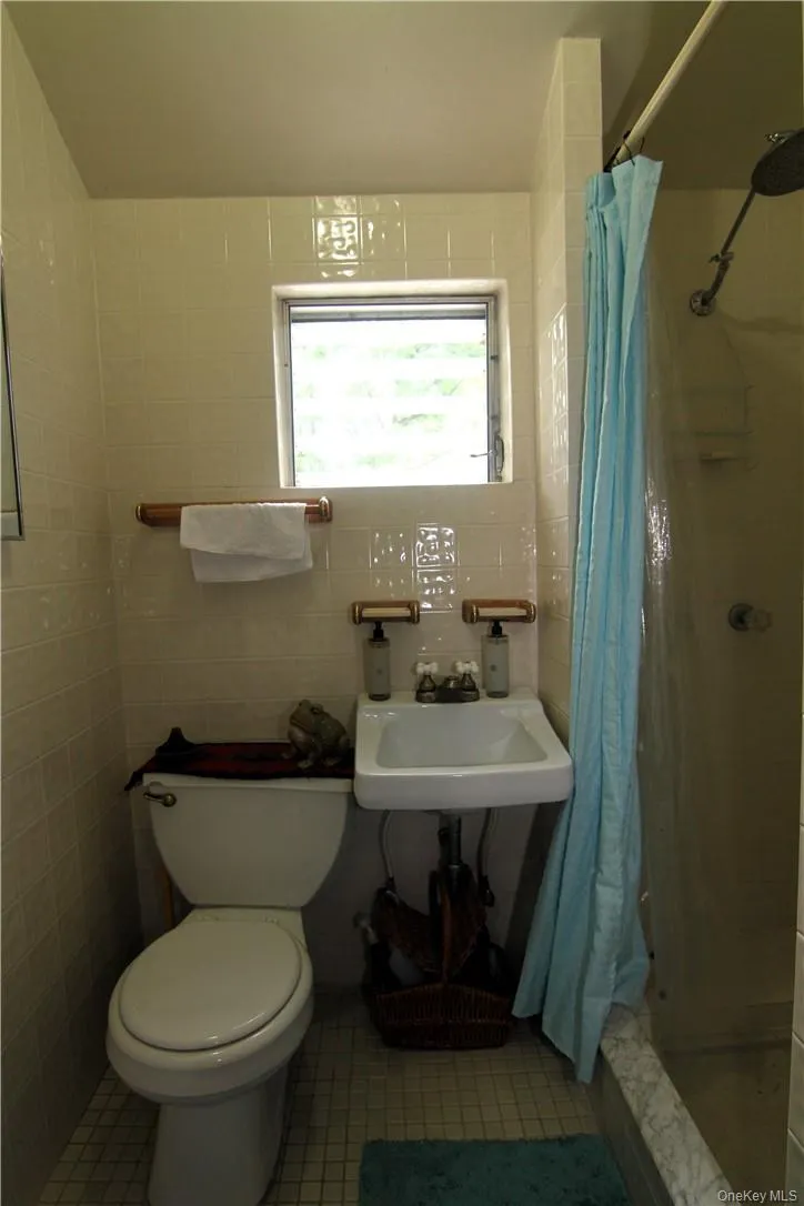 Bathroom featuring tile walls, toilet, tile floors, curtained shower, and sink Bathroom featuring tile walls, toilet, tile floors, curtained shower, and sink