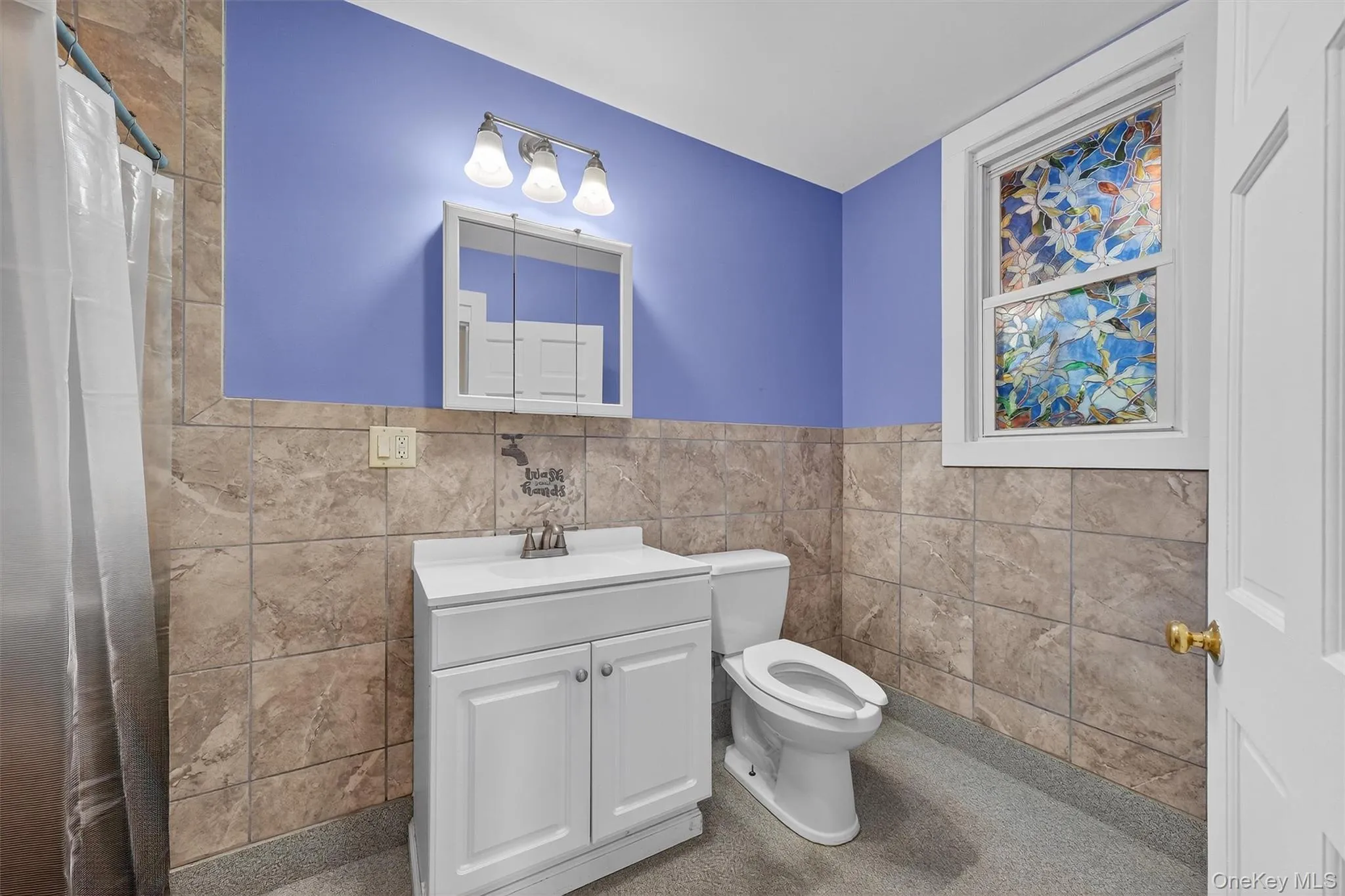 Bathroom with vanity, tile walls, curtained shower, and a wainscoted wall Bathroom with vanity, tile walls, curtained shower, and a wainscoted wall