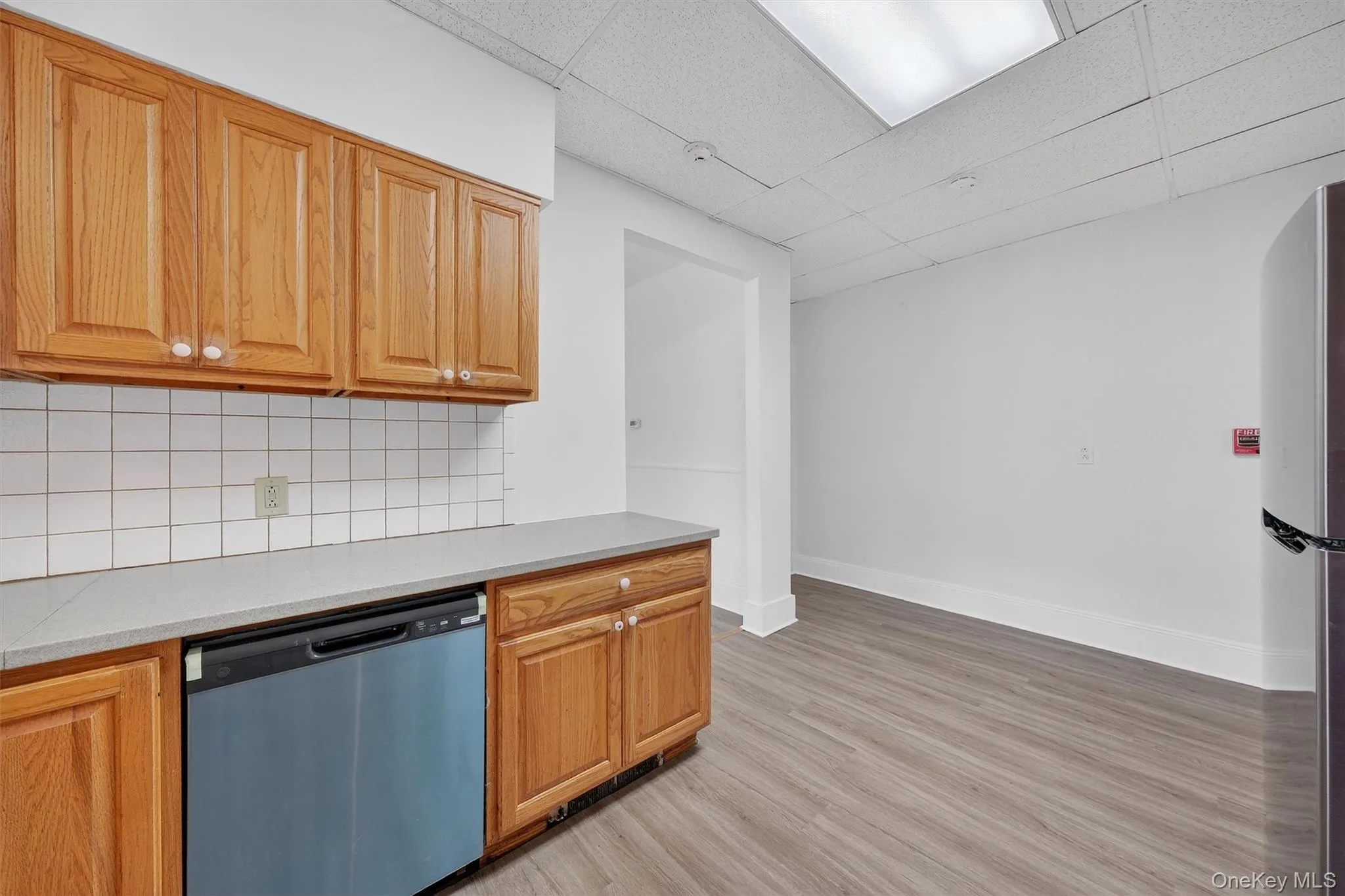 Kitchen featuring a drop ceiling, decorative backsplash, appliances with stainless steel finishes, light wood-type flooring, and light countertops Kitchen featuring a drop ceiling, decorative backsplash, appliances with stainless steel finishes, light wood-type flooring, and light countertops