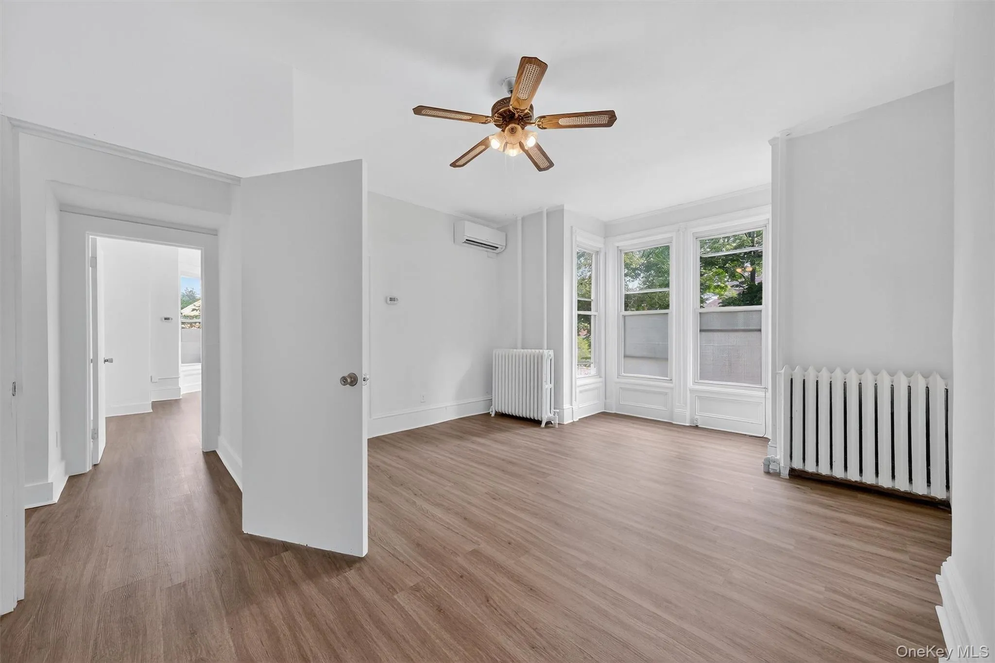 Empty room featuring radiator, wood finished floors, a ceiling fan, and a wall unit AC Empty room featuring radiator, wood finished floors, a ceiling fan, and a wall unit AC