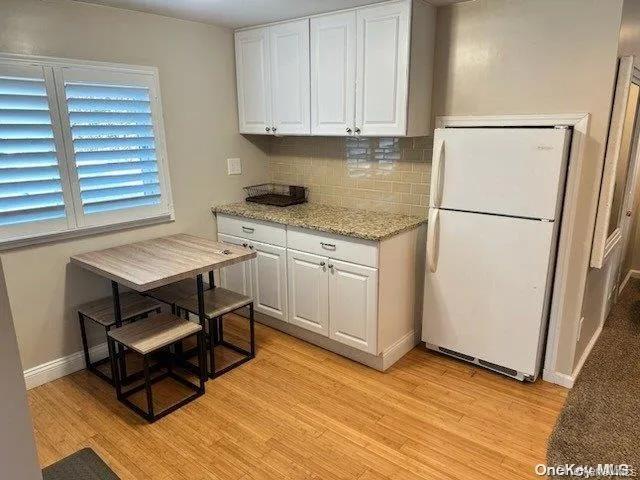 Kitchen with light stone counters, white cabinets, freestanding refrigerator, decorative backsplash, and light wood finished floors Kitchen with light stone counters, white cabinets, freestanding refrigerator, decorative backsplash, and light wood finished floors