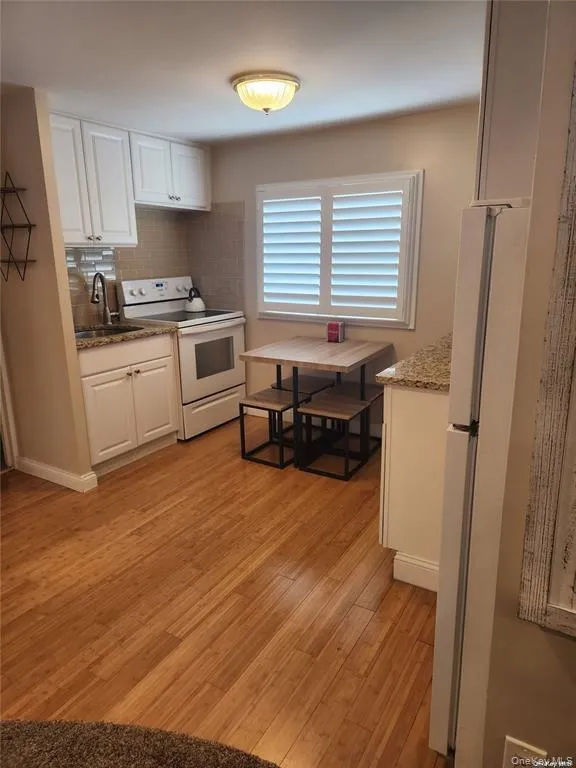 Kitchen featuring white appliances, a sink, white cabinetry, backsplash, and light wood finished floors Kitchen featuring white appliances, a sink, white cabinetry, backsplash, and light wood finished floors