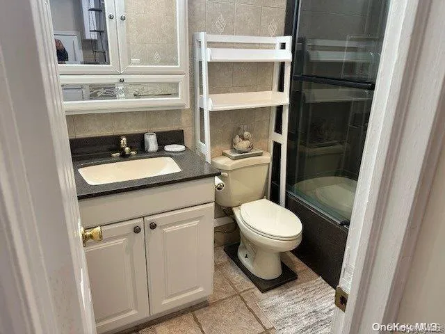 Bathroom featuring tasteful backsplash, toilet, tile patterned flooring, vanity, and tile walls Bathroom featuring tasteful backsplash, toilet, tile patterned flooring, vanity, and tile walls