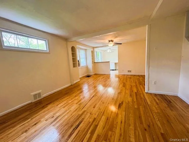 Hardwood flooring throughout a spacious room with Built-in shelving, a large horizontal Window, and a Dining Room Hardwood flooring throughout a spacious room with Built-in shelving, a large horizontal Window, and a Dining Room
