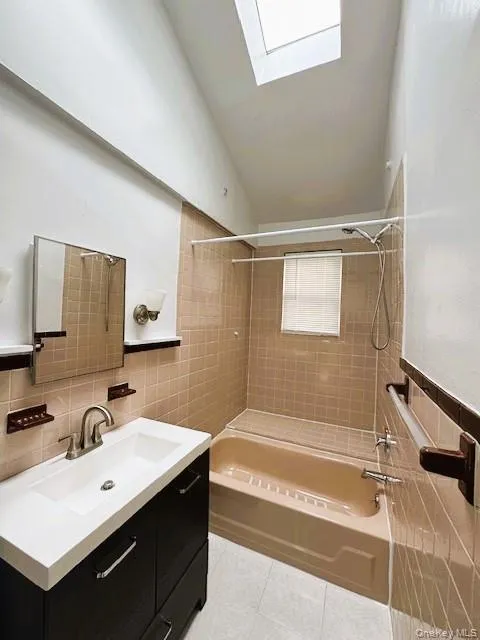 Bathroom featuring a skylight, a dark-finish vanity with a white countertop, a mirror, and a beige tiled shower/tub combination Bathroom featuring a skylight, a dark-finish vanity with a white countertop, a mirror, and a beige tiled shower/tub combination