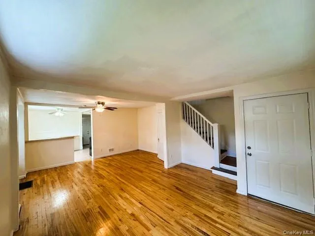Hardwood flooring in a spacious room featuring a white paneled entry door and a staircase with white balusters Hardwood flooring in a spacious room featuring a white paneled entry door and a staircase with white balusters