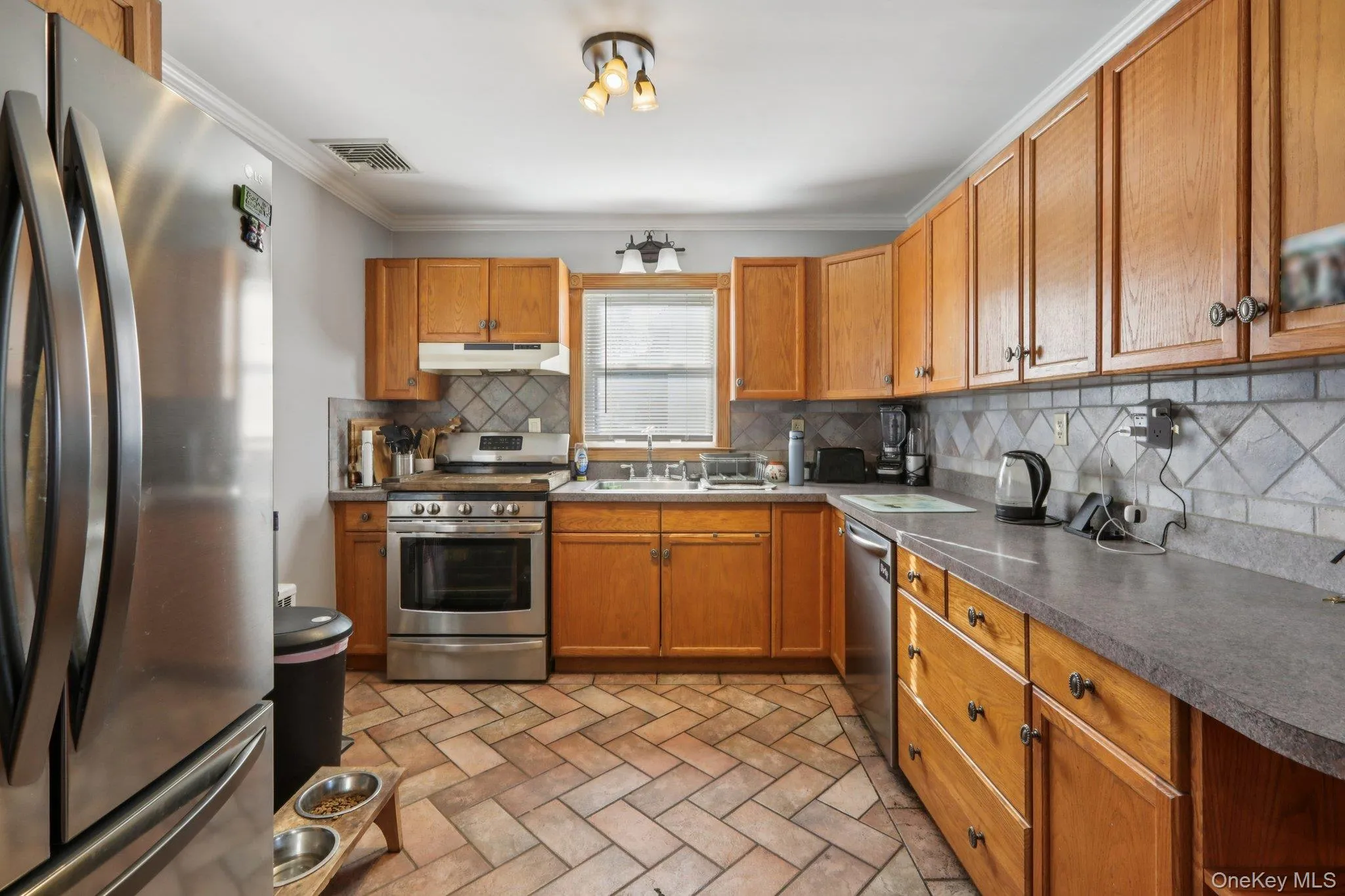 Kitchen with stainless steel appliances, wood finish cabinets, dark countertops, crown molding, and decorative backsplash Kitchen with stainless steel appliances, wood finish cabinets, dark countertops, crown molding, and decorative backsplash