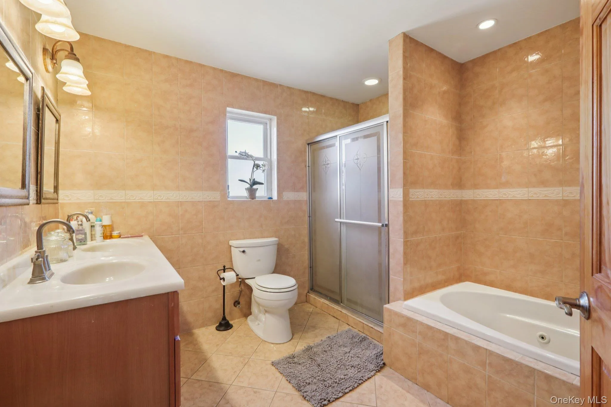 Bathroom with tile walls, double vanity, light tile patterned floors, a bath, and a shower stall Bathroom with tile walls, double vanity, light tile patterned floors, a bath, and a shower stall