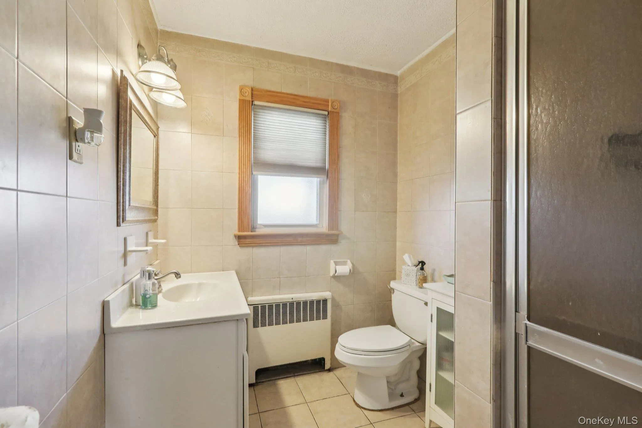Full bathroom with radiator heating unit, vanity, a stall shower, light tile patterned floors, and tile walls Full bathroom with radiator heating unit, vanity, a stall shower, light tile patterned floors, and tile walls