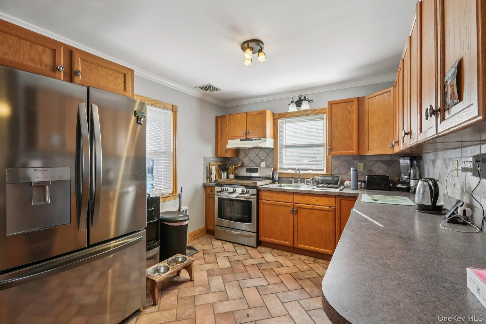 Kitchen with stainless steel appliances, wood finish cabinets, dark countertops, ornamental molding, and decorative backsplash Kitchen with stainless steel appliances, wood finish cabinets, dark countertops, ornamental molding, and decorative backsplash