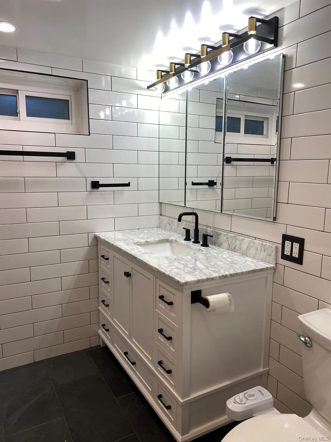 The bathroom featuring tile walls, vanity, and dark tile Flooring The bathroom featuring tile walls, vanity, and dark tile Flooring