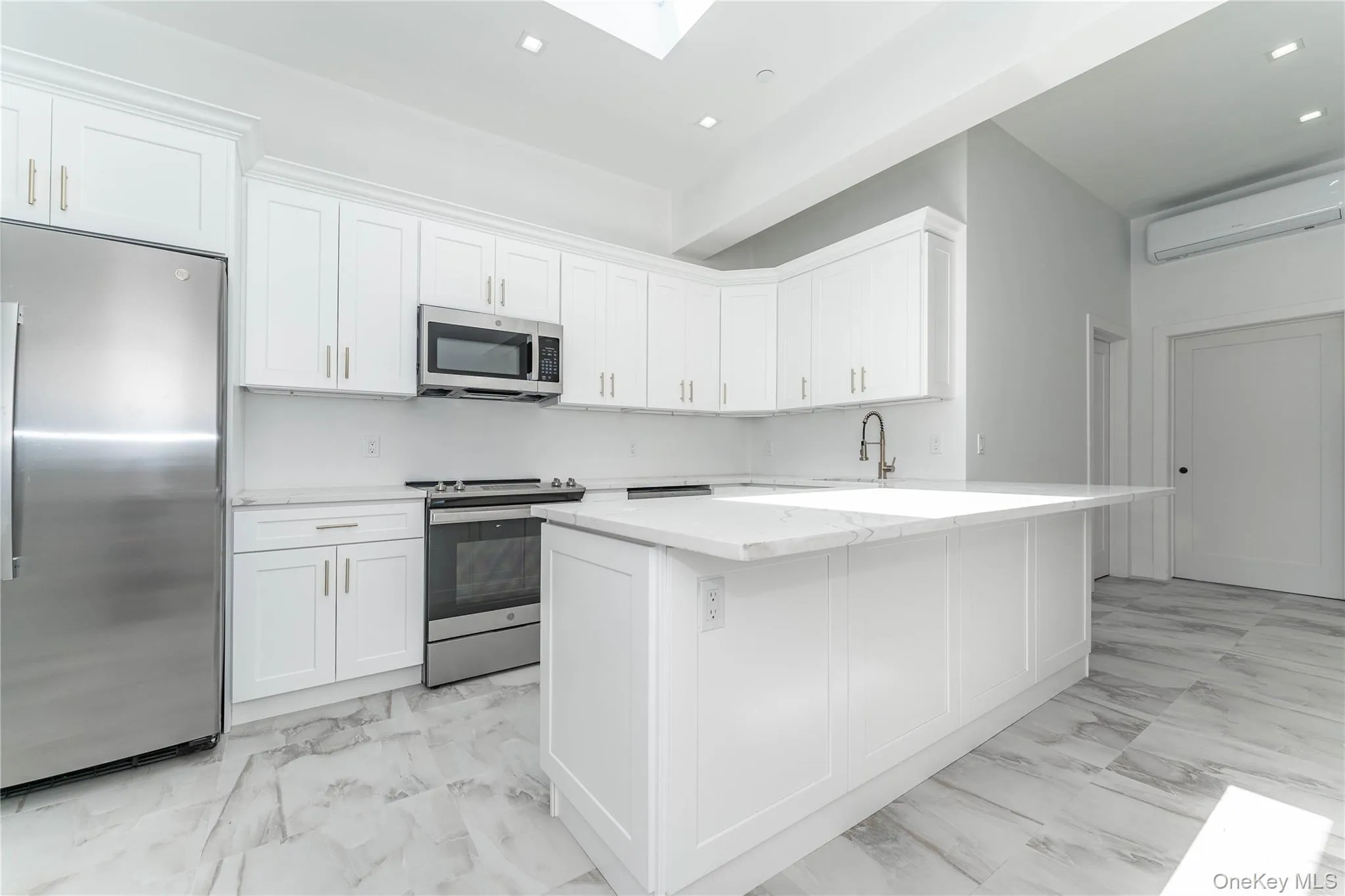 Kitchen with stainless steel appliances, a wall mounted air conditioner, light marble finish flooring, a skylight, and white cabinets Kitchen with stainless steel appliances, a wall mounted air conditioner, light marble finish flooring, a skylight, and white cabinets