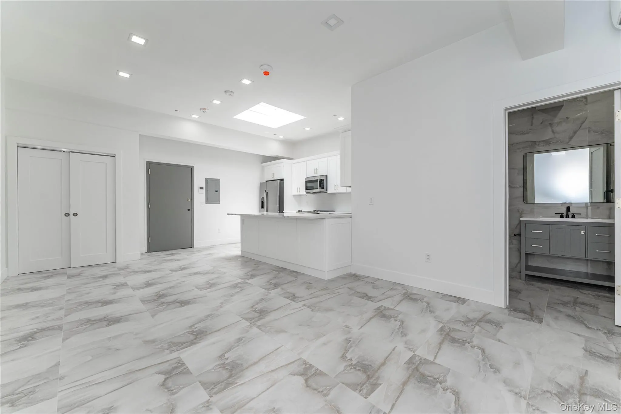 Unfurnished living room featuring light marble finish flooring, a skylight, a sink, baseboards, and recessed lighting Unfurnished living room featuring light marble finish flooring, a skylight, a sink, baseboards, and recessed lighting
