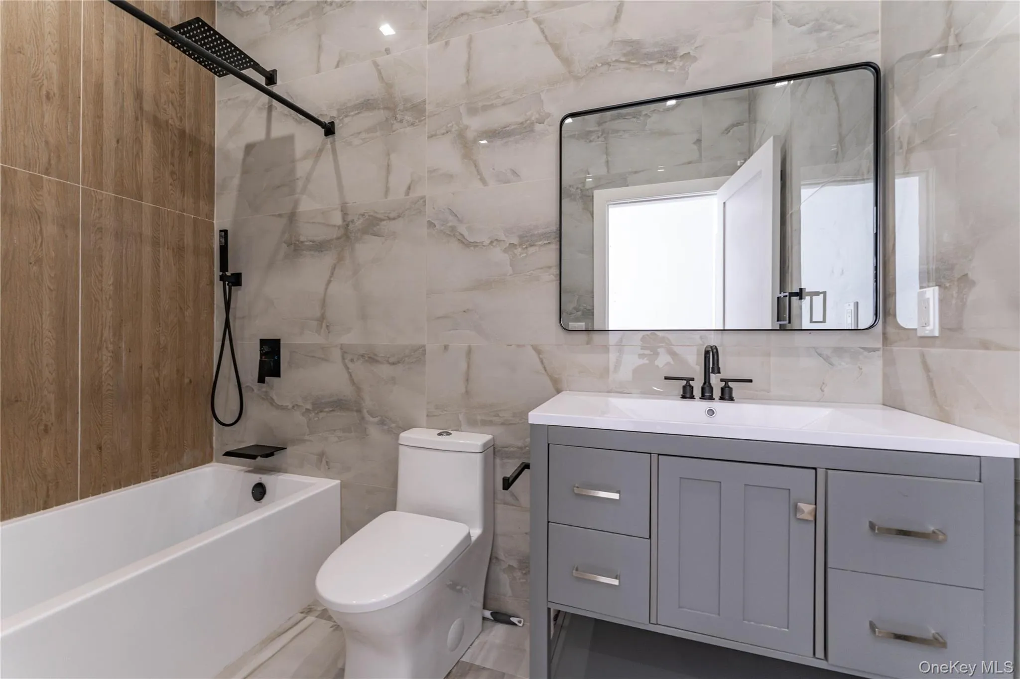 Bathroom featuring tile walls, vanity, toilet, tasteful backsplash, and washtub / shower combination Bathroom featuring tile walls, vanity, toilet, tasteful backsplash, and washtub / shower combination