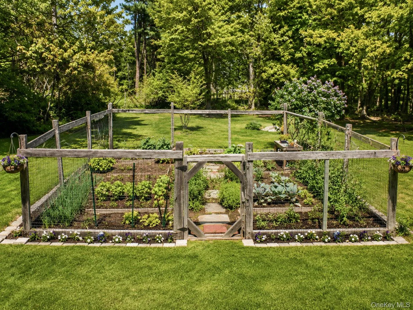 Fenced garden enclosure featuring a custom wooden gate, ready for planting beds, and a perimeter of decorative flowers Fenced garden enclosure featuring a custom wooden gate, ready for planting beds, and a perimeter of decorative flowers