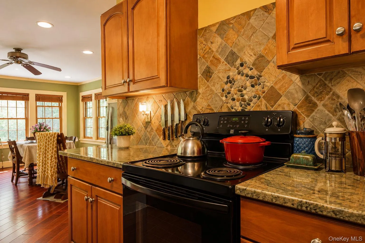 Kitchen featuring wood cabinetry, granite countertops, and a stone tile backsplash with a pebble inlay Kitchen featuring wood cabinetry, granite countertops, and a stone tile backsplash with a pebble inlay