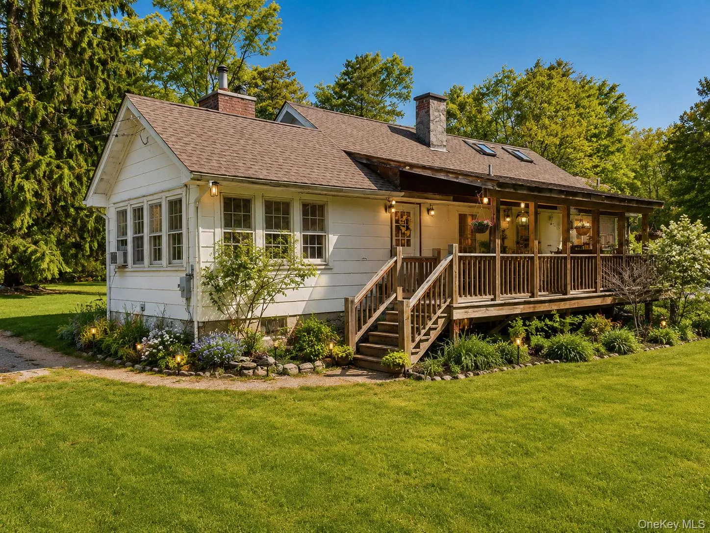 Angled view of the residence featuring a spacious wood deck, multiple skylights, a brick chimney, mature trees, and a manicured lawn Angled view of the residence featuring a spacious wood deck, multiple skylights, a brick chimney, mature trees, and a manicured lawn
