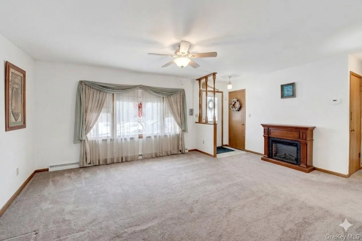 Unfurnished living room with a ceiling fan, a fireplace, carpet, and a baseboard heating unit Unfurnished living room with a ceiling fan, a fireplace, carpet, and a baseboard heating unit
