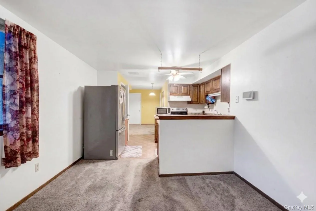 Kitchen featuring wood finish cabinetry, stainless steel appliances, light carpet, a peninsula, and ceiling fan Kitchen featuring wood finish cabinetry, stainless steel appliances, light carpet, a peninsula, and ceiling fan
