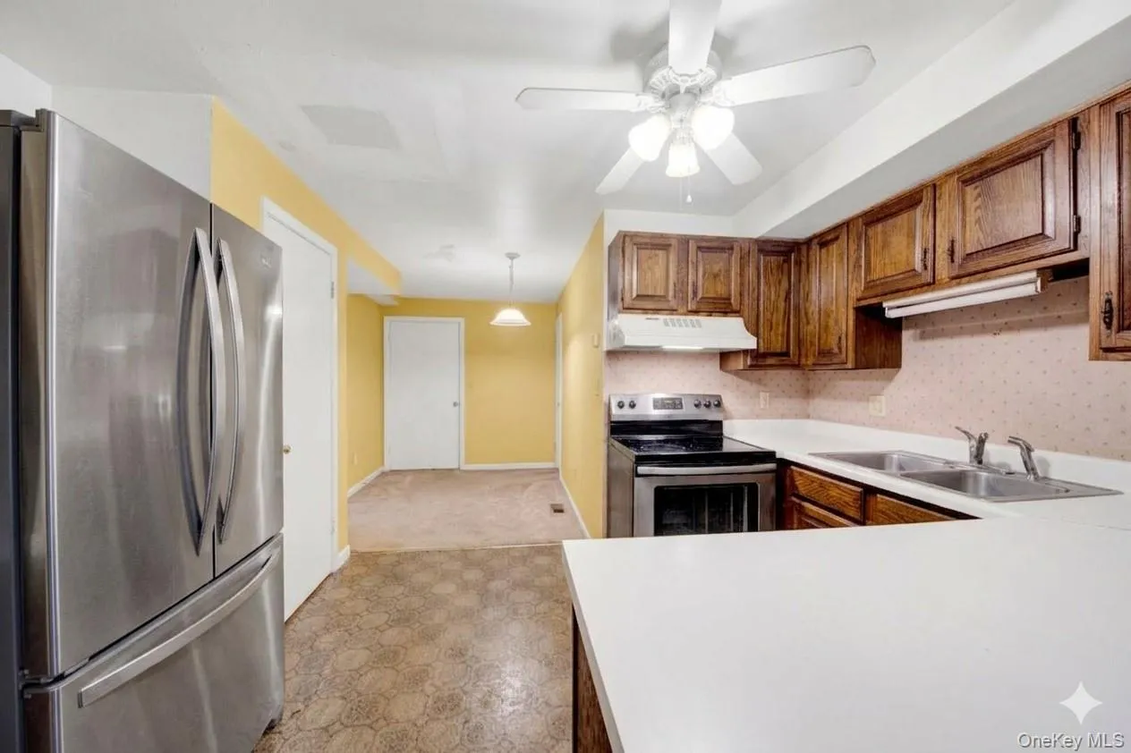 Kitchen featuring stainless steel appliances, light countertops, a ceiling fan, wood finish cabinetry, and light floors Kitchen featuring stainless steel appliances, light countertops, a ceiling fan, wood finish cabinetry, and light floors